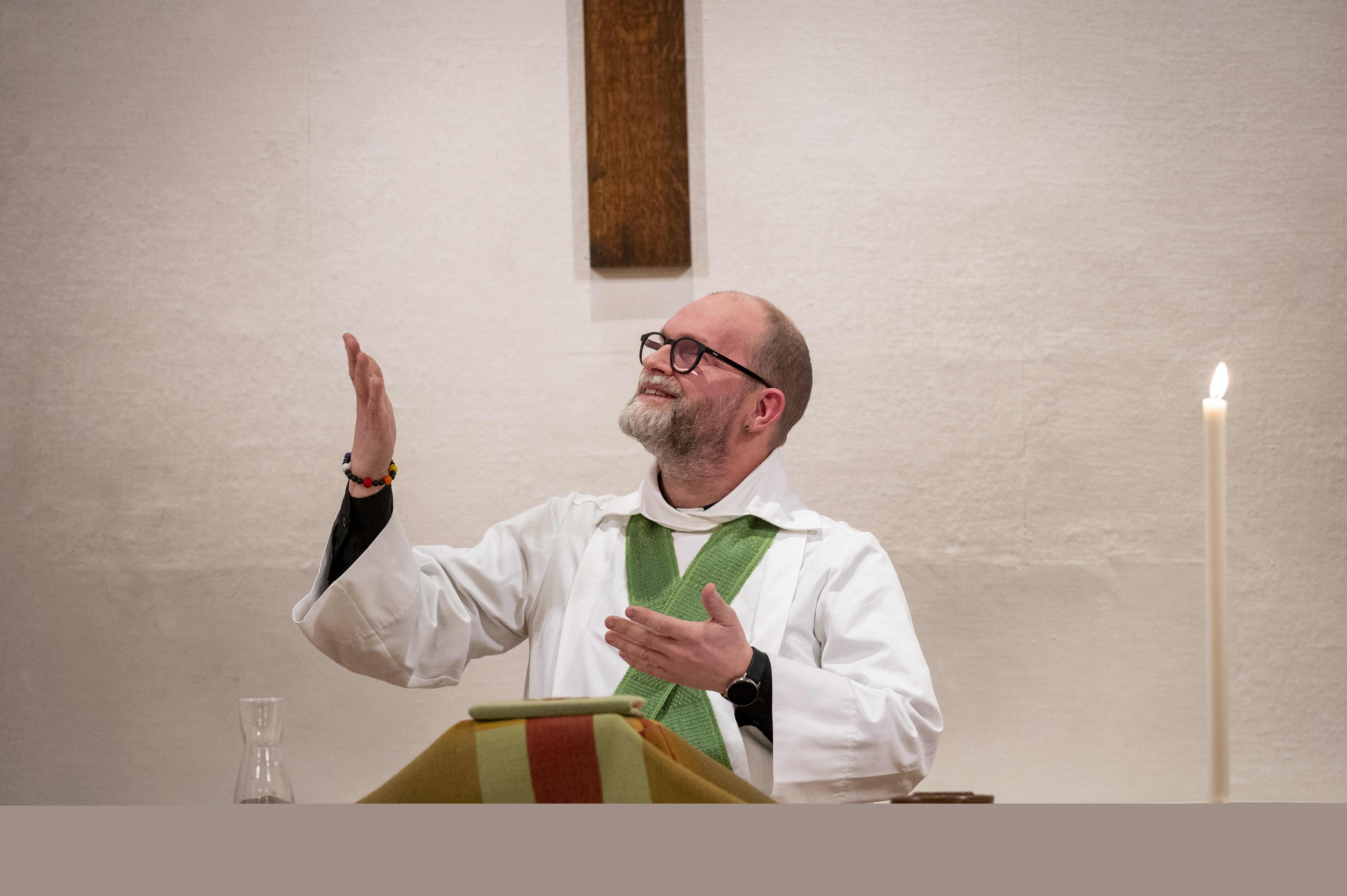 En manlig präst står vid altaret och gestikulerar med armarna.
