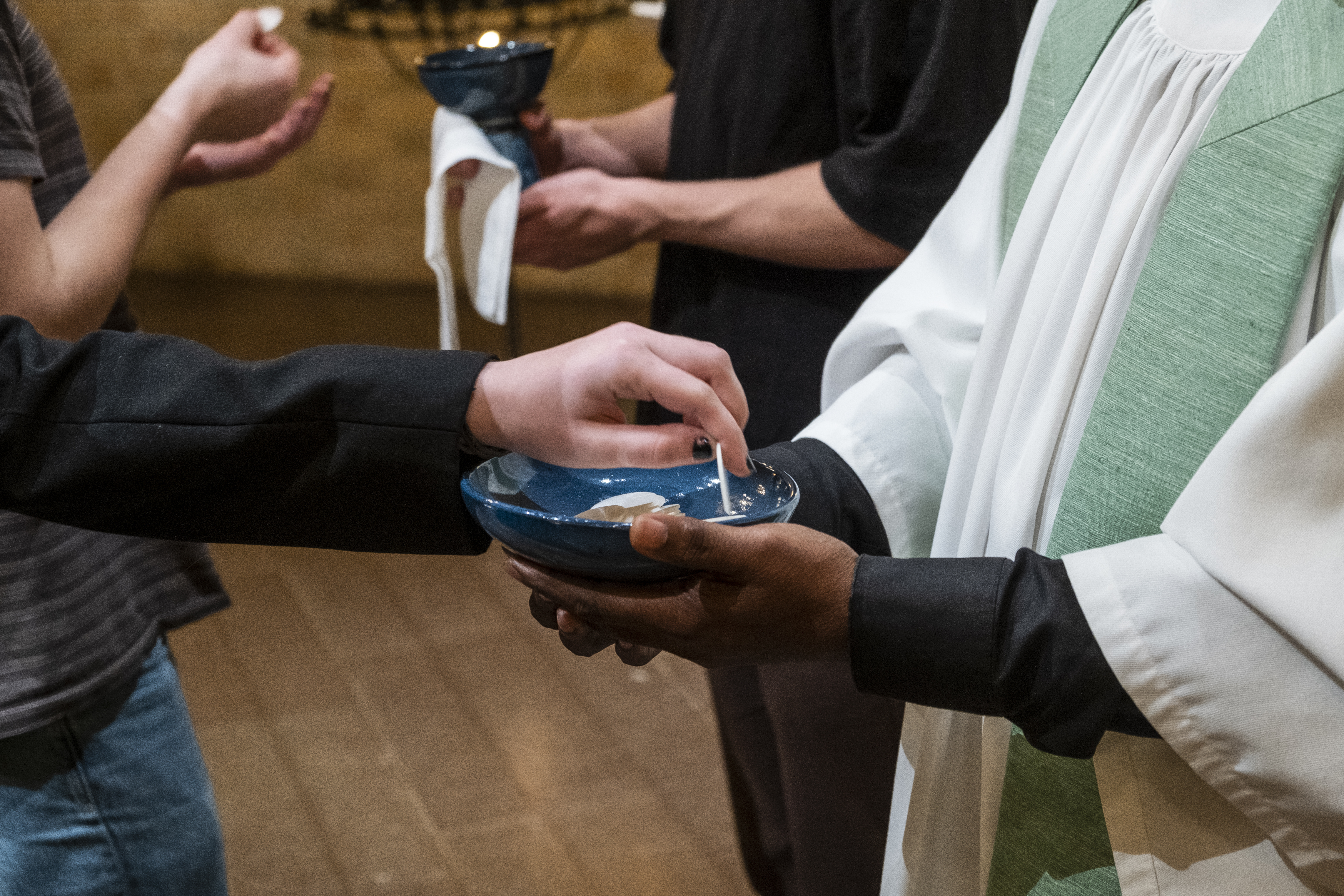 Någon tar en oblat från en skål prästen håller fram.
