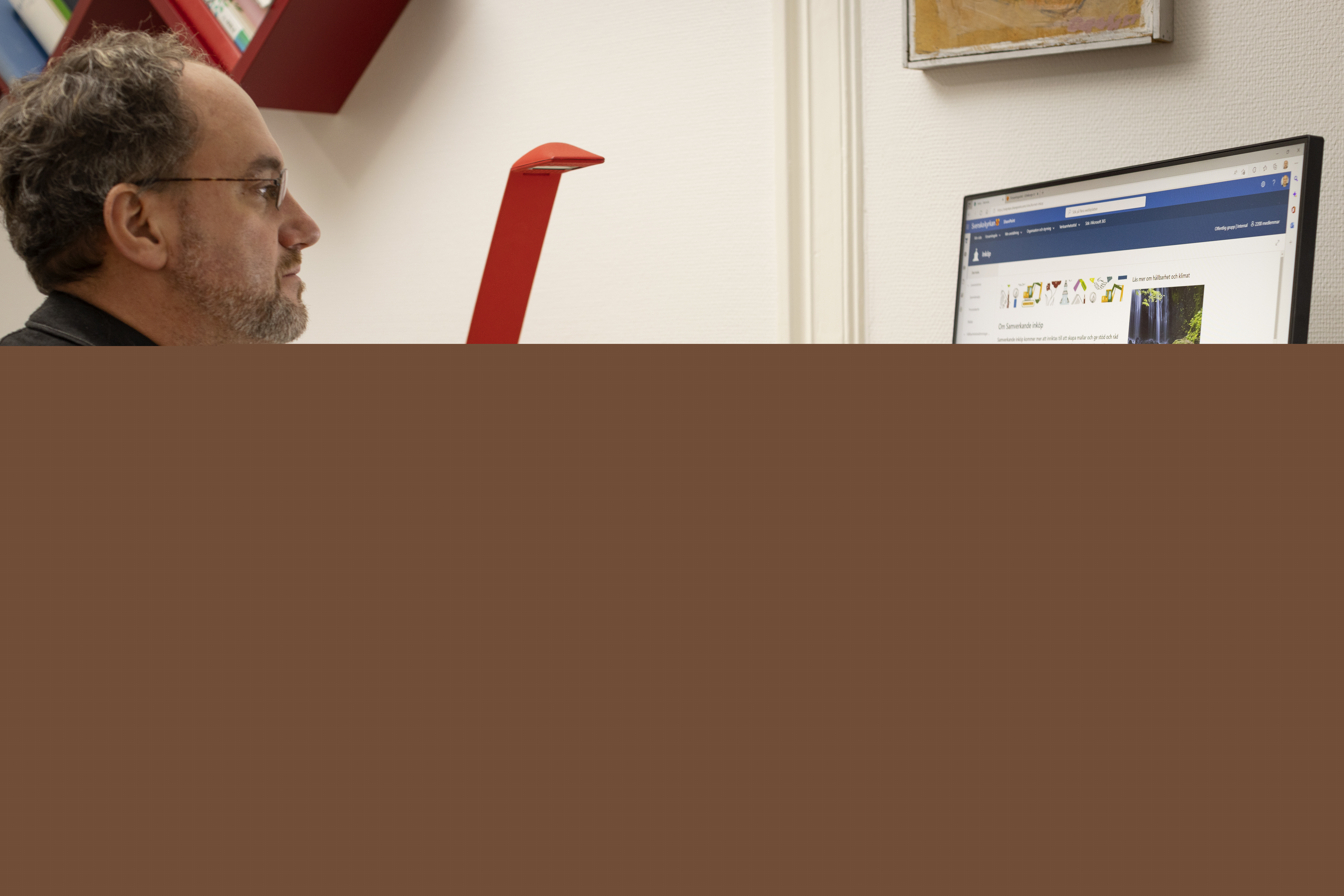 En man sitter vid ett skrivbord och arbetar i datorn.