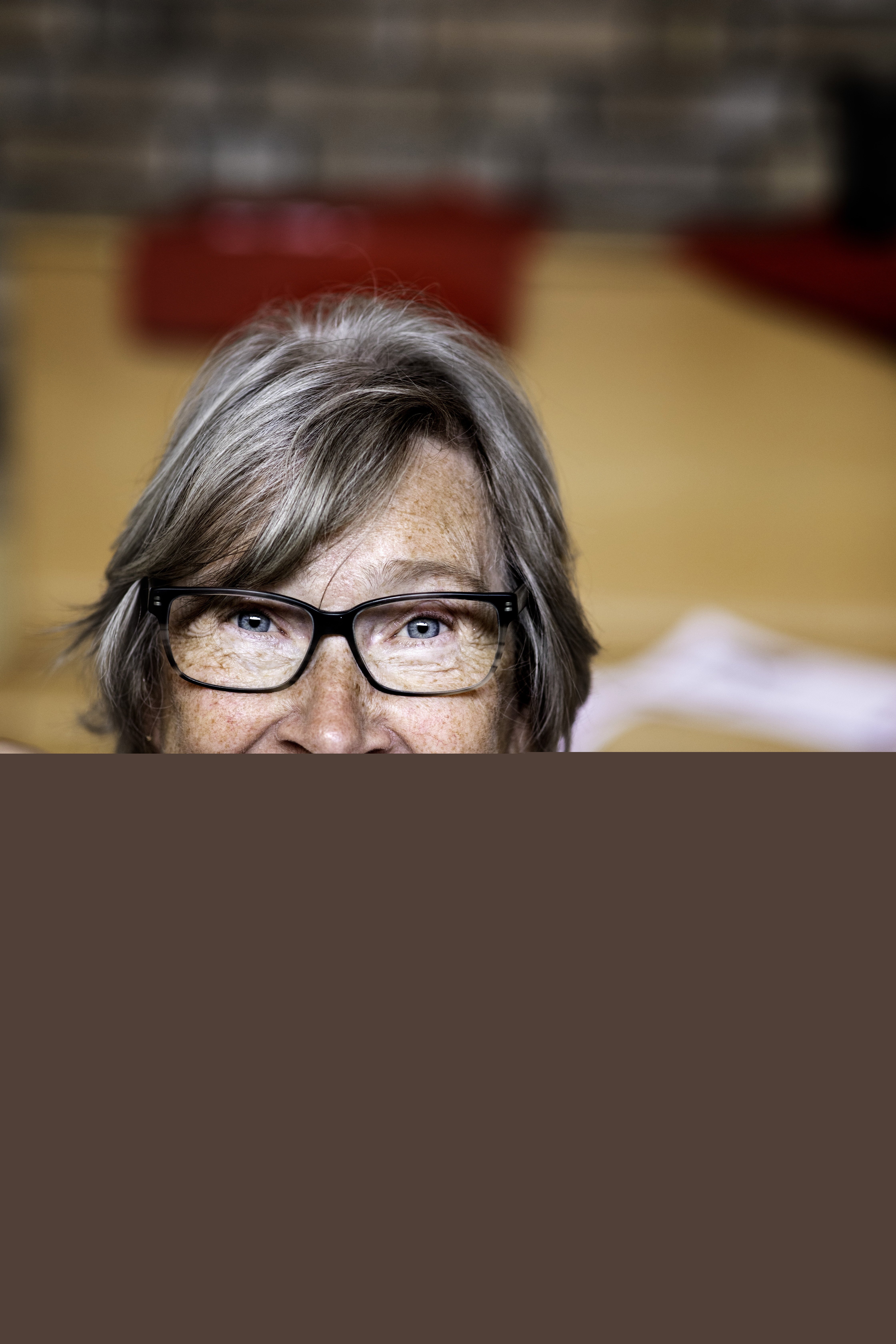 En kvinna med glasögon och färgglad blus håller upp en vit och blå stickning mot kameran.