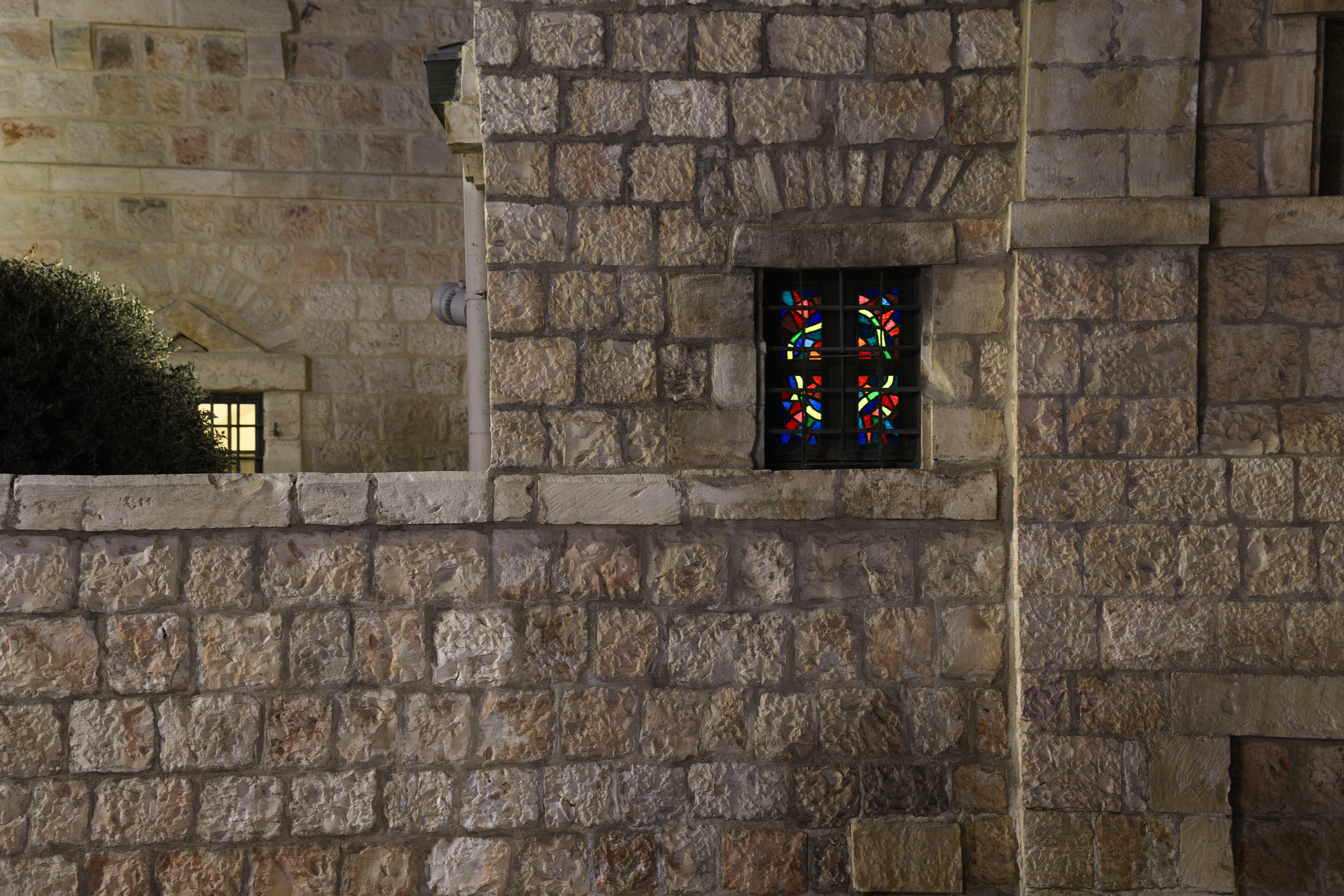 Närbild på ett litet fönster i vackra färger insprängt i en rejäl stenmur.