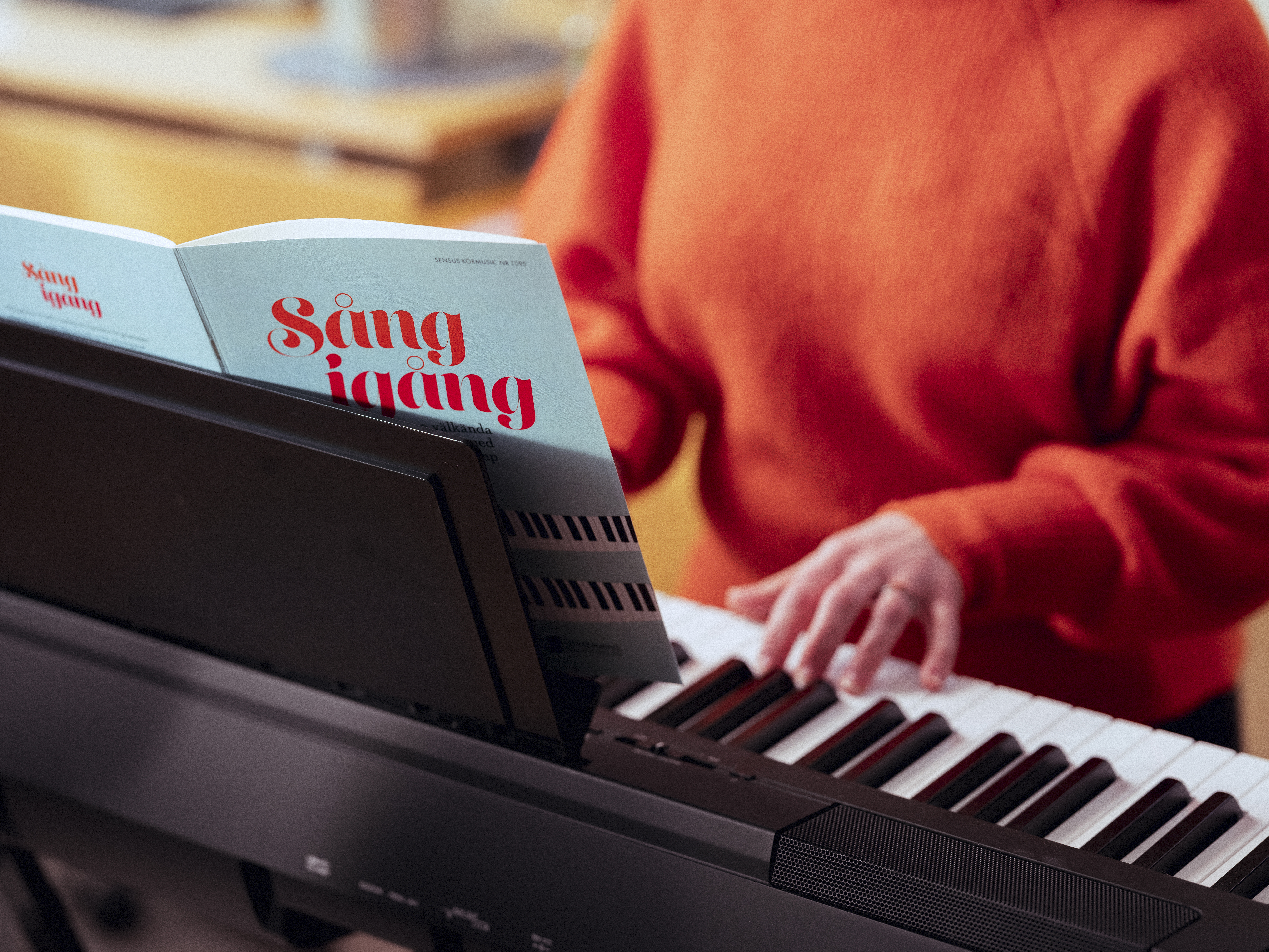 Någon i en orange stickad tröja sitter och spelar keyboard.