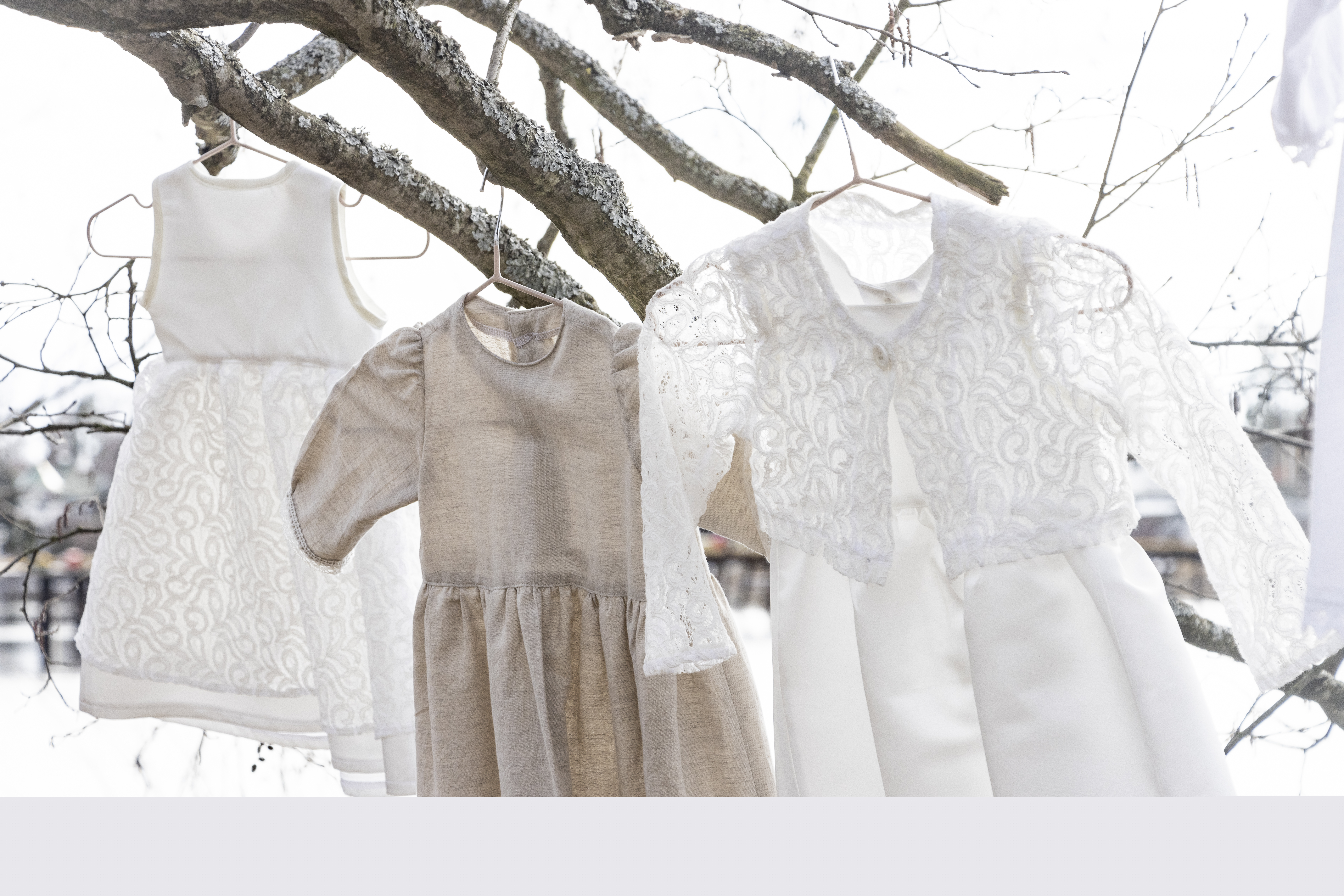 Tre olika dopklänningar hänger i ett träds grenar.
