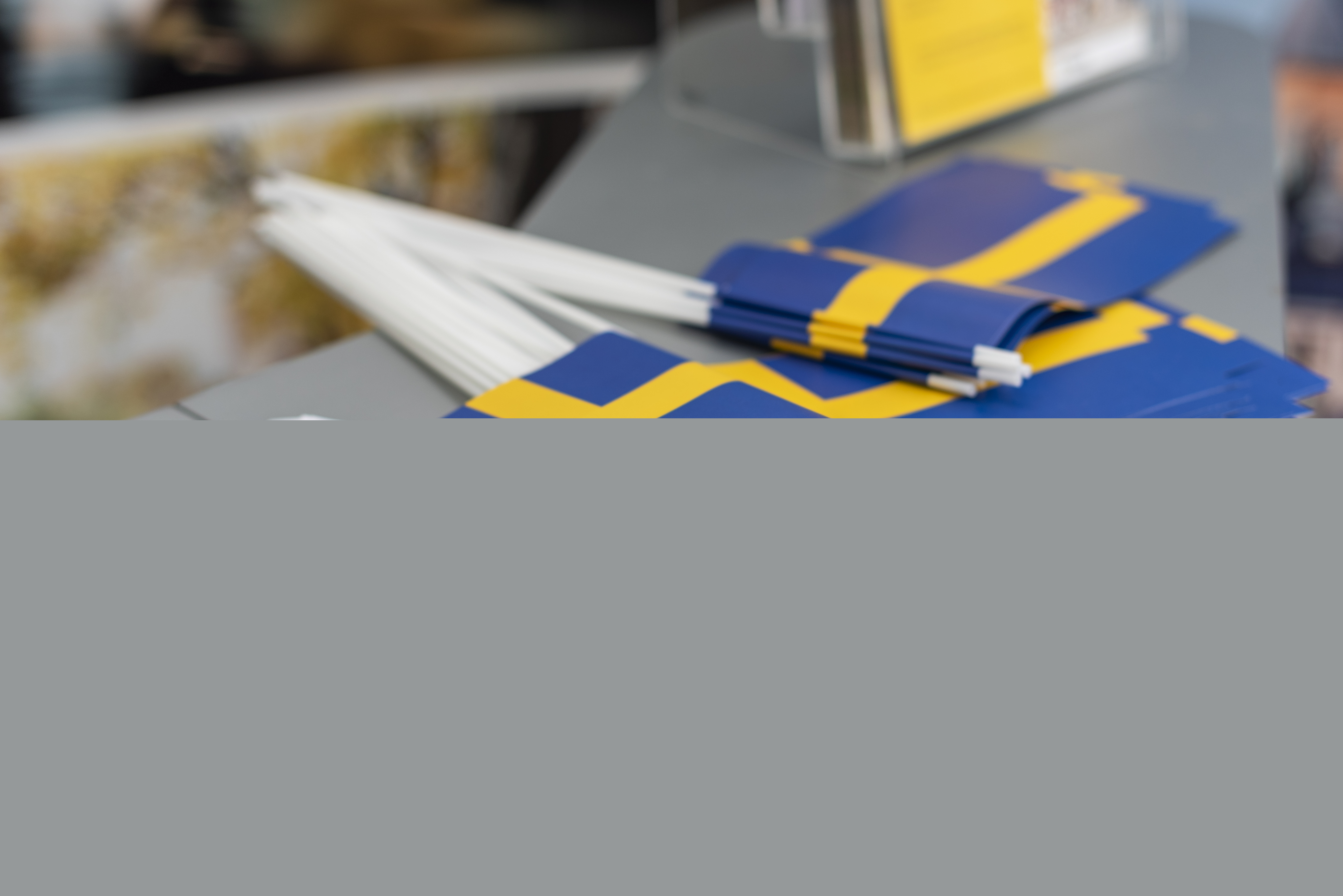 En hög med svenska flaggor och tryckta blad med texten Sveriges nationaldag ligger på en bänkyta.