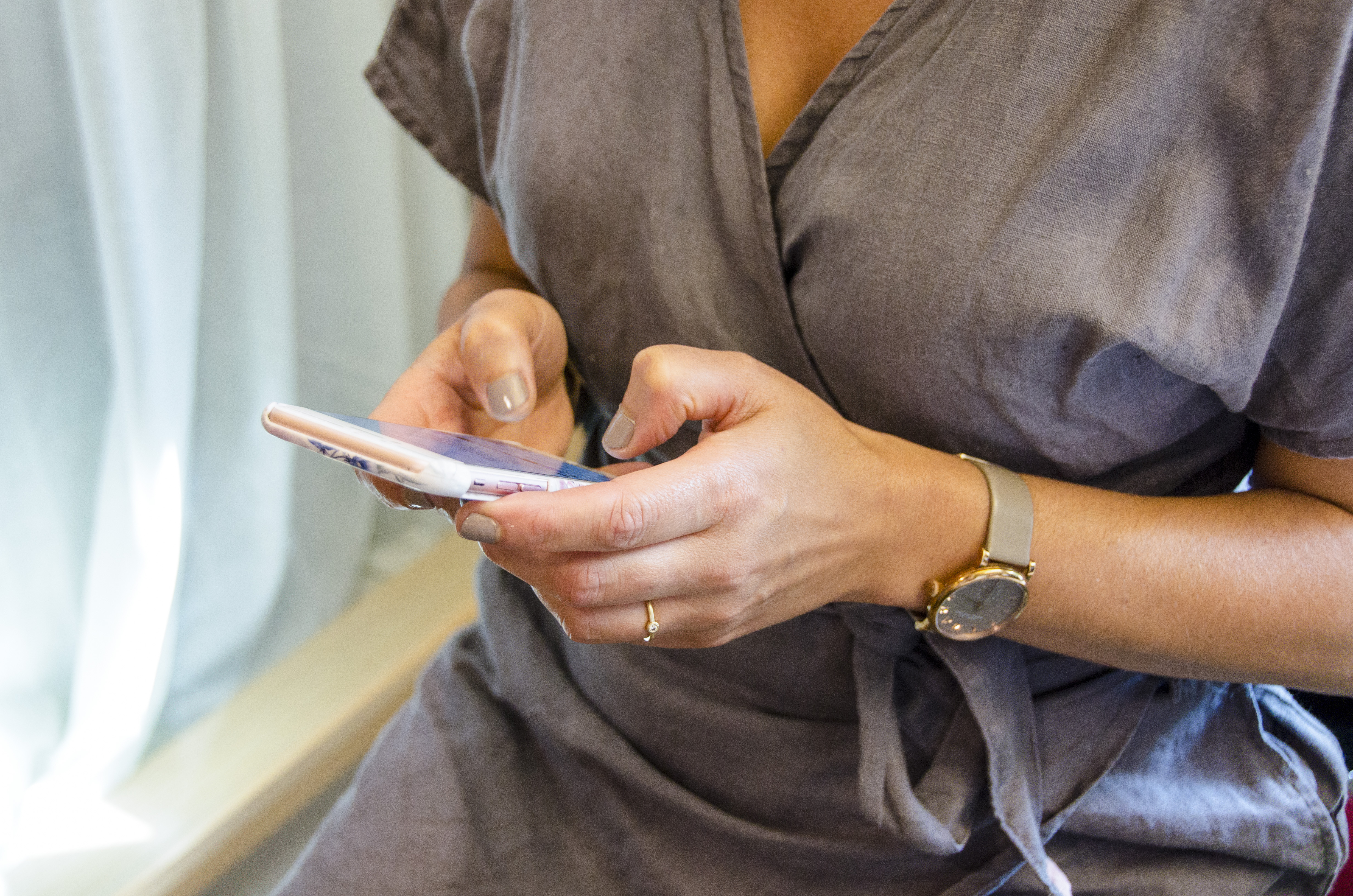 En kvinna med grå blus knappar på en smartphone.