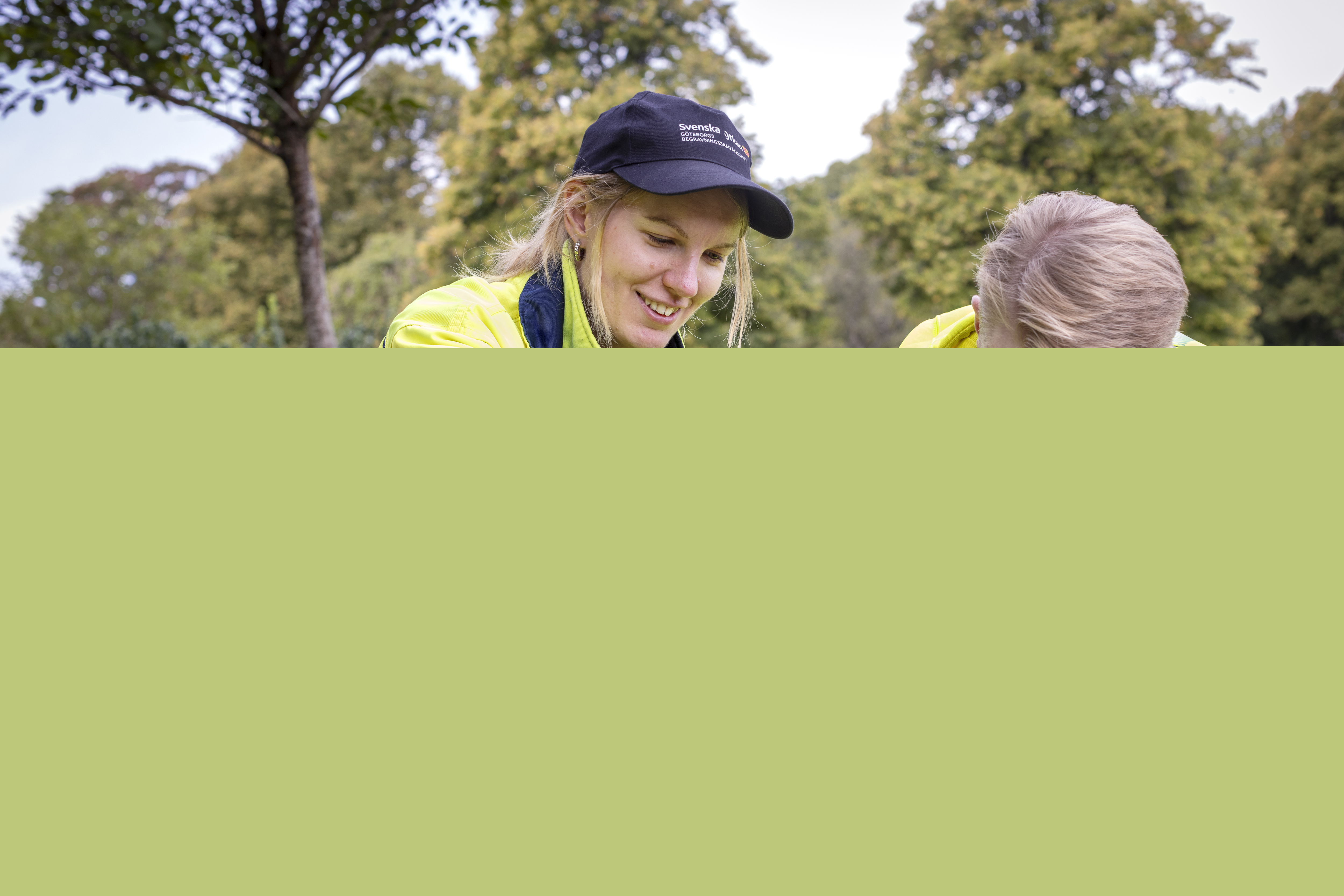 Två kyrkogårdsarbetare i gula varselkläder fixar med några blommor.