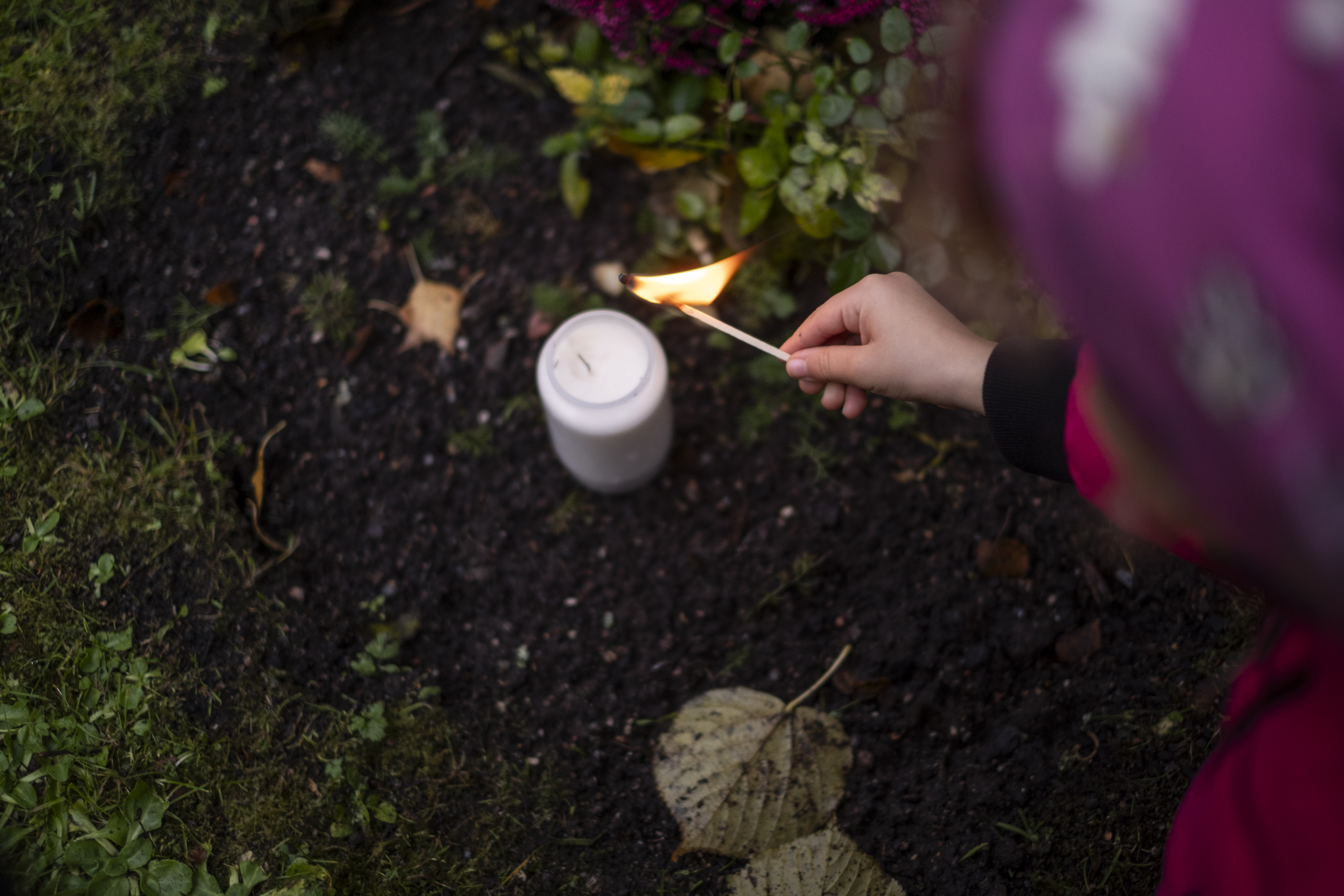 Ett litet barn tänder ett ljus vid en gravplats.