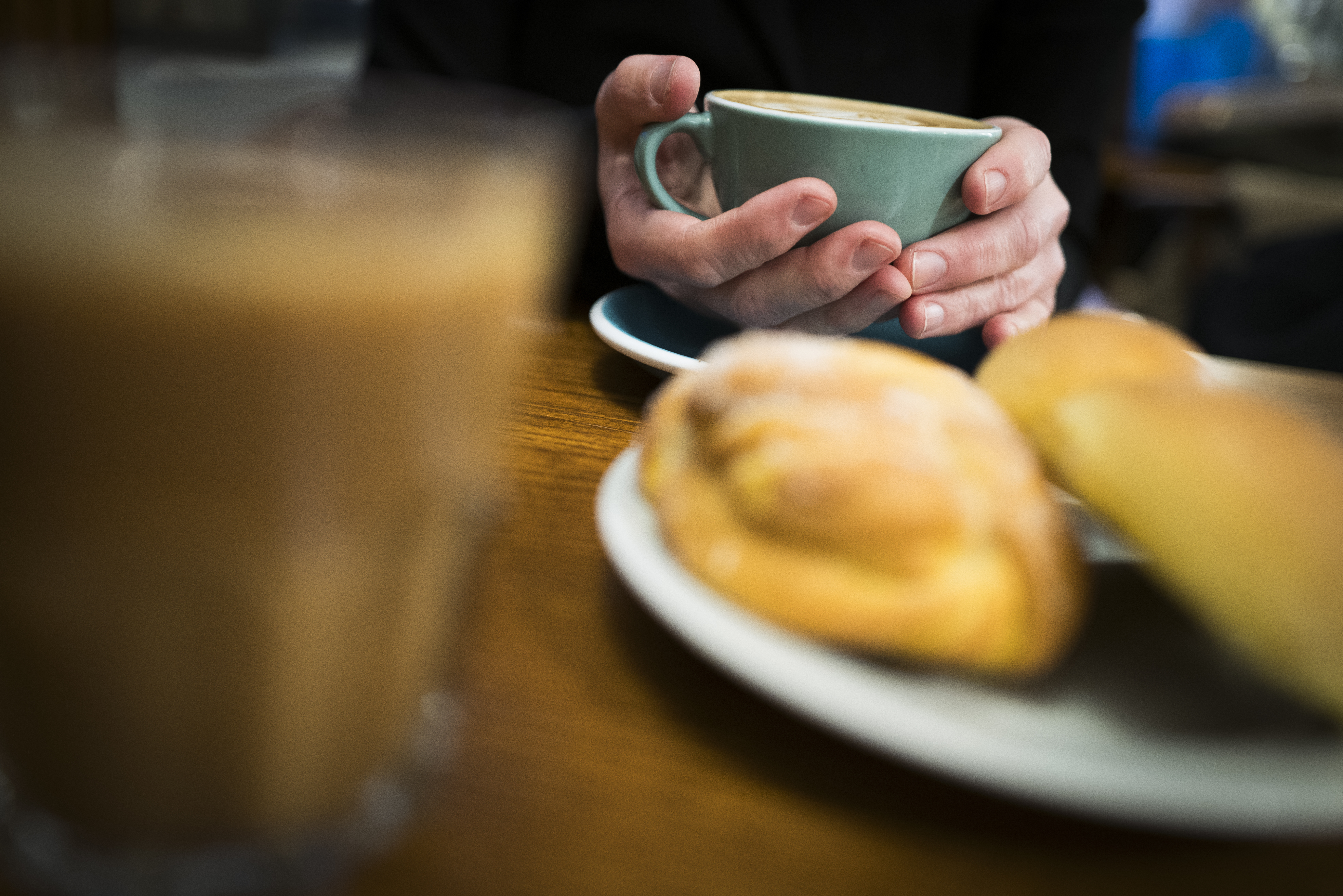 En kupad hand håller en grön kaffekopp. Bullar på ett fat i förgrunden.