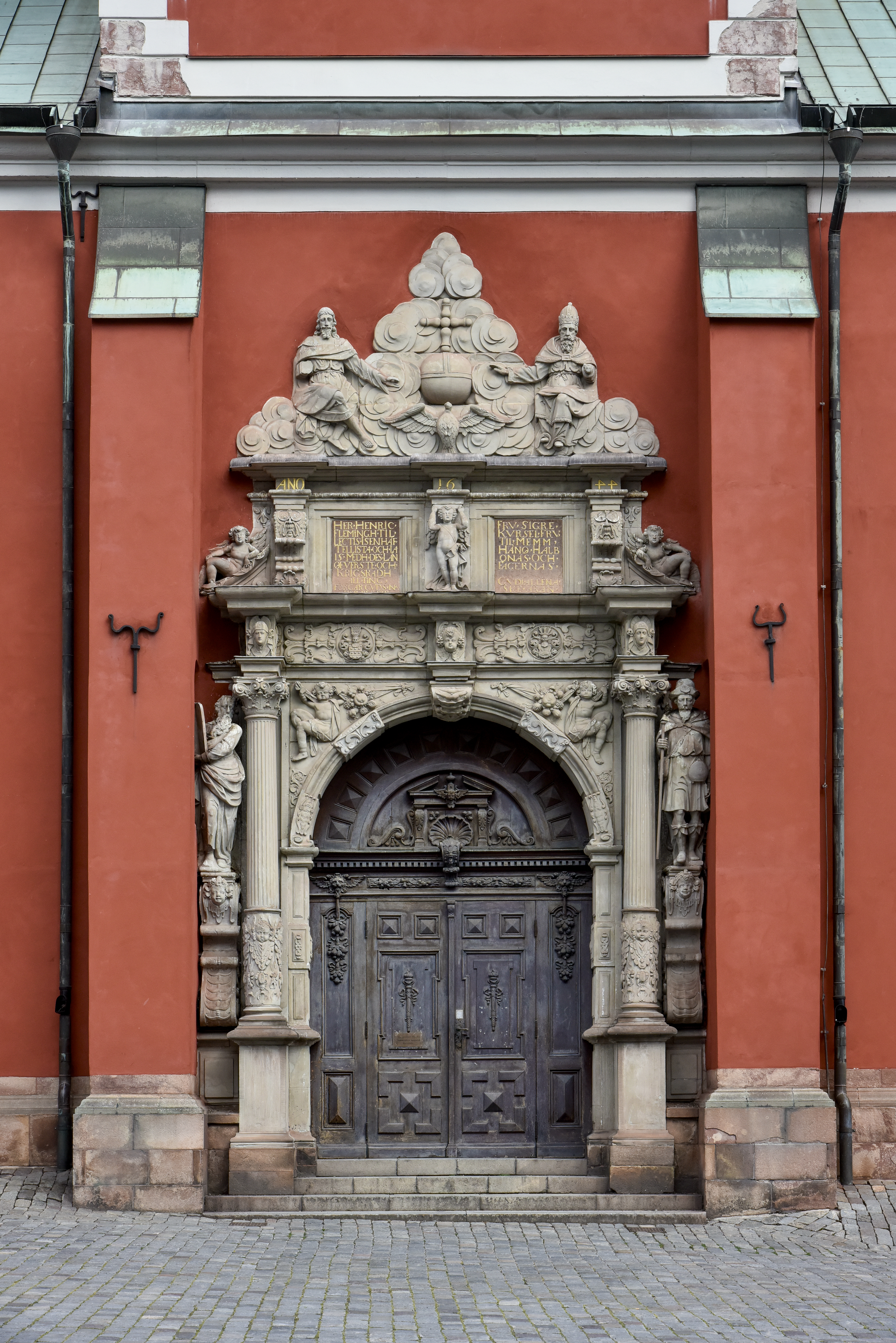En mörk träport omgiven av marmorutsmyckning på en rödputsad kyrka.