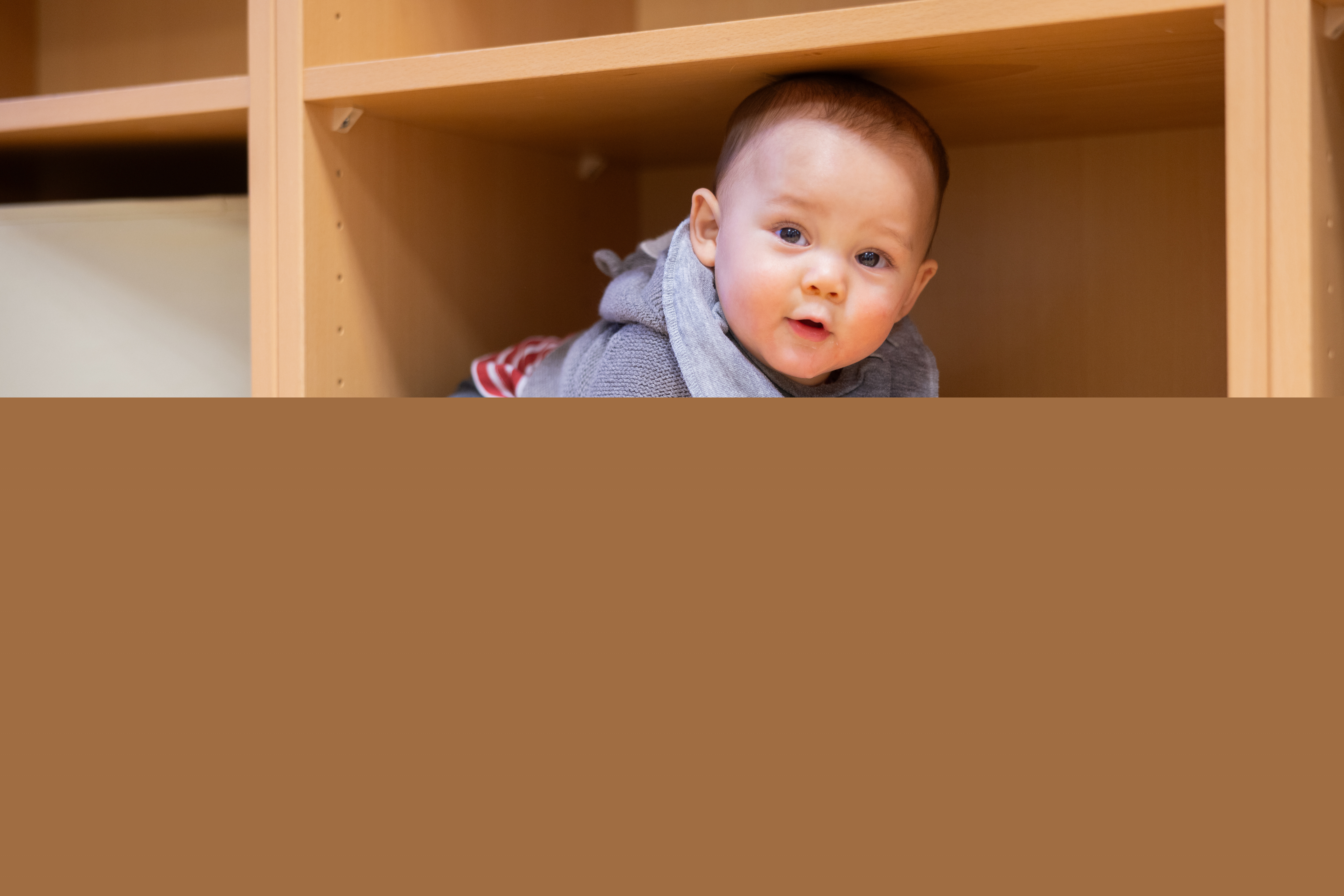 En bebis har klättrat in i en tom bokhylla.