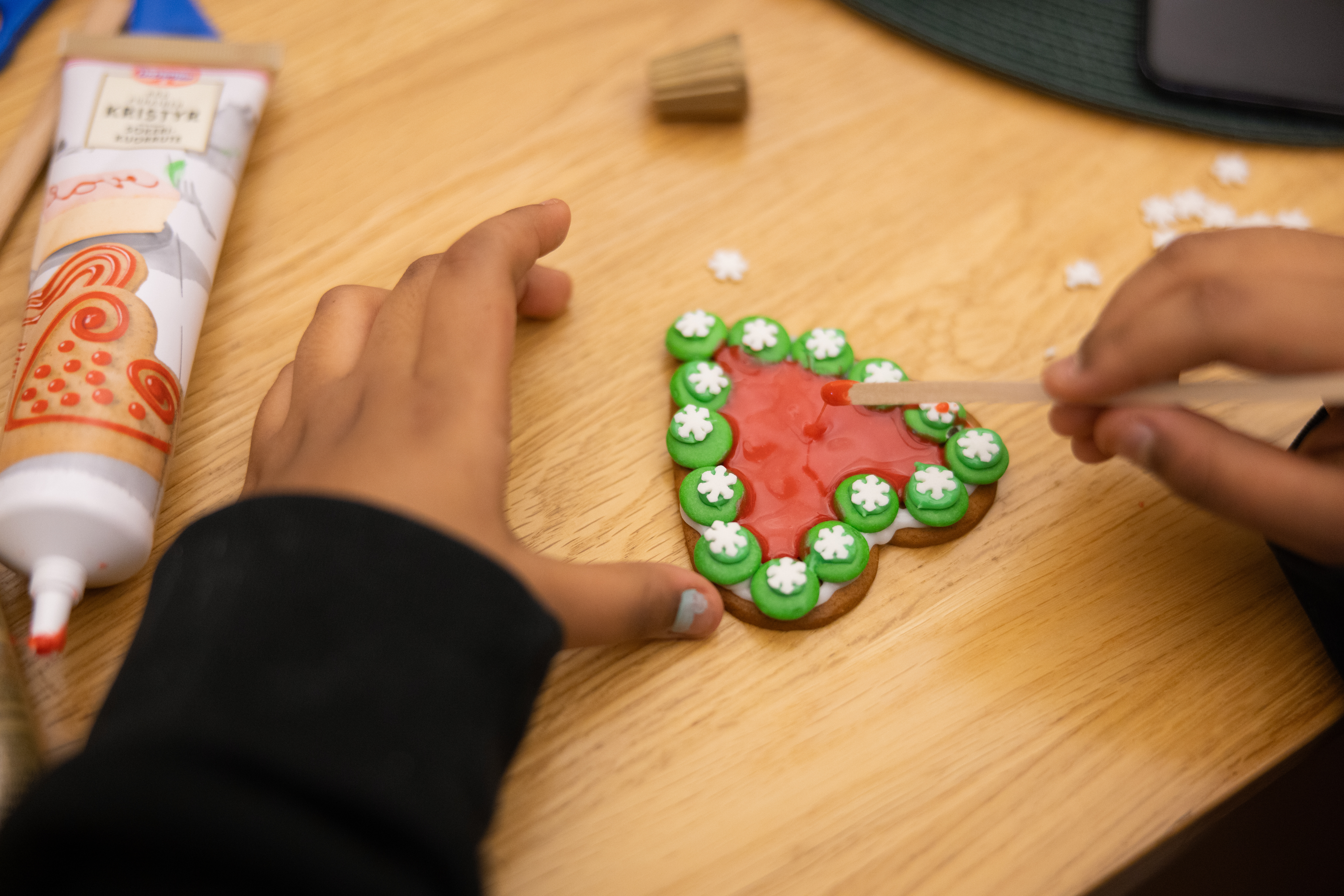 Närbild på ett barns händer som lagt non stop och kristyr på ett pepparkakshjärta.