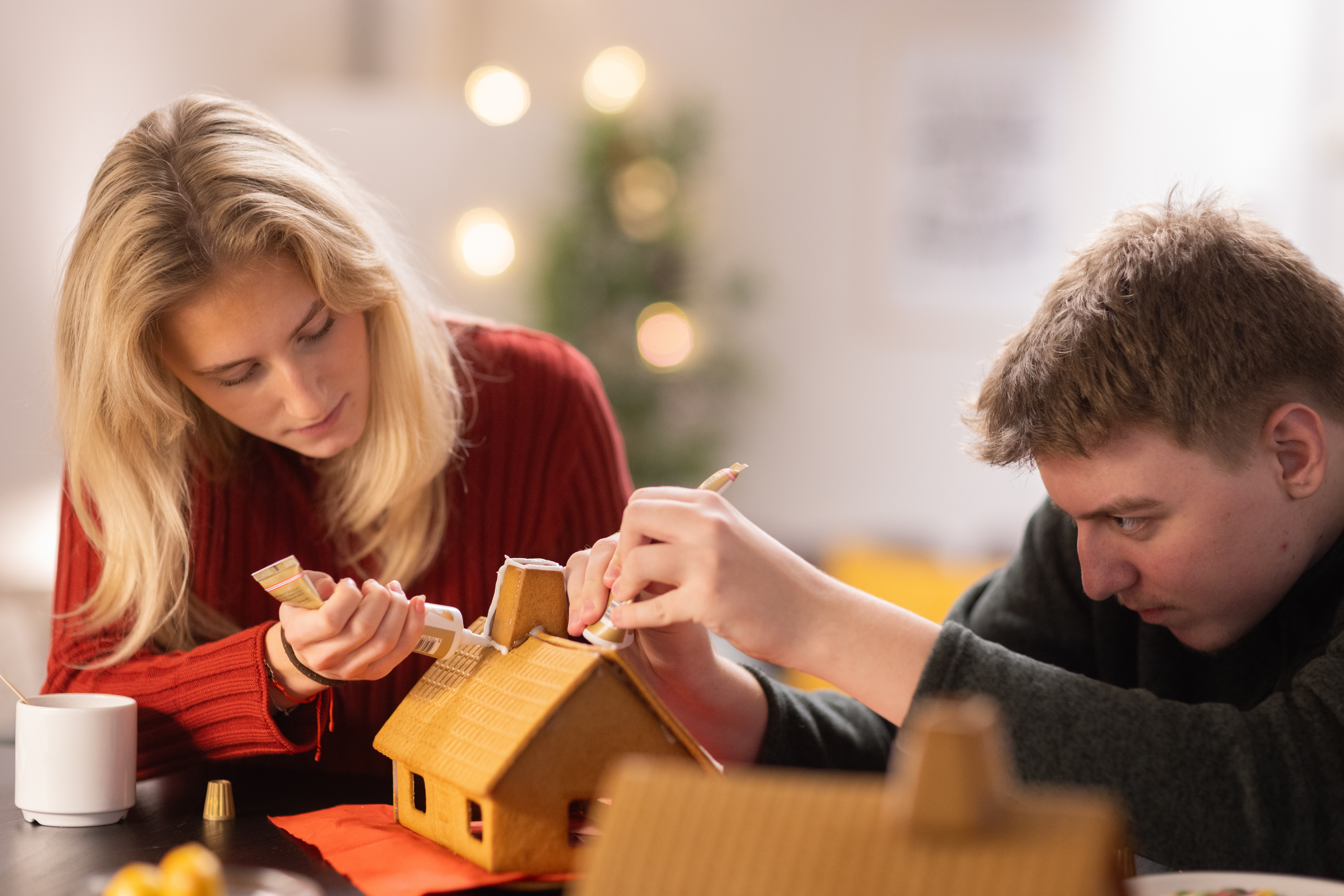 En tjej och en kille i tonåren spritsar ett pepparkakshus.