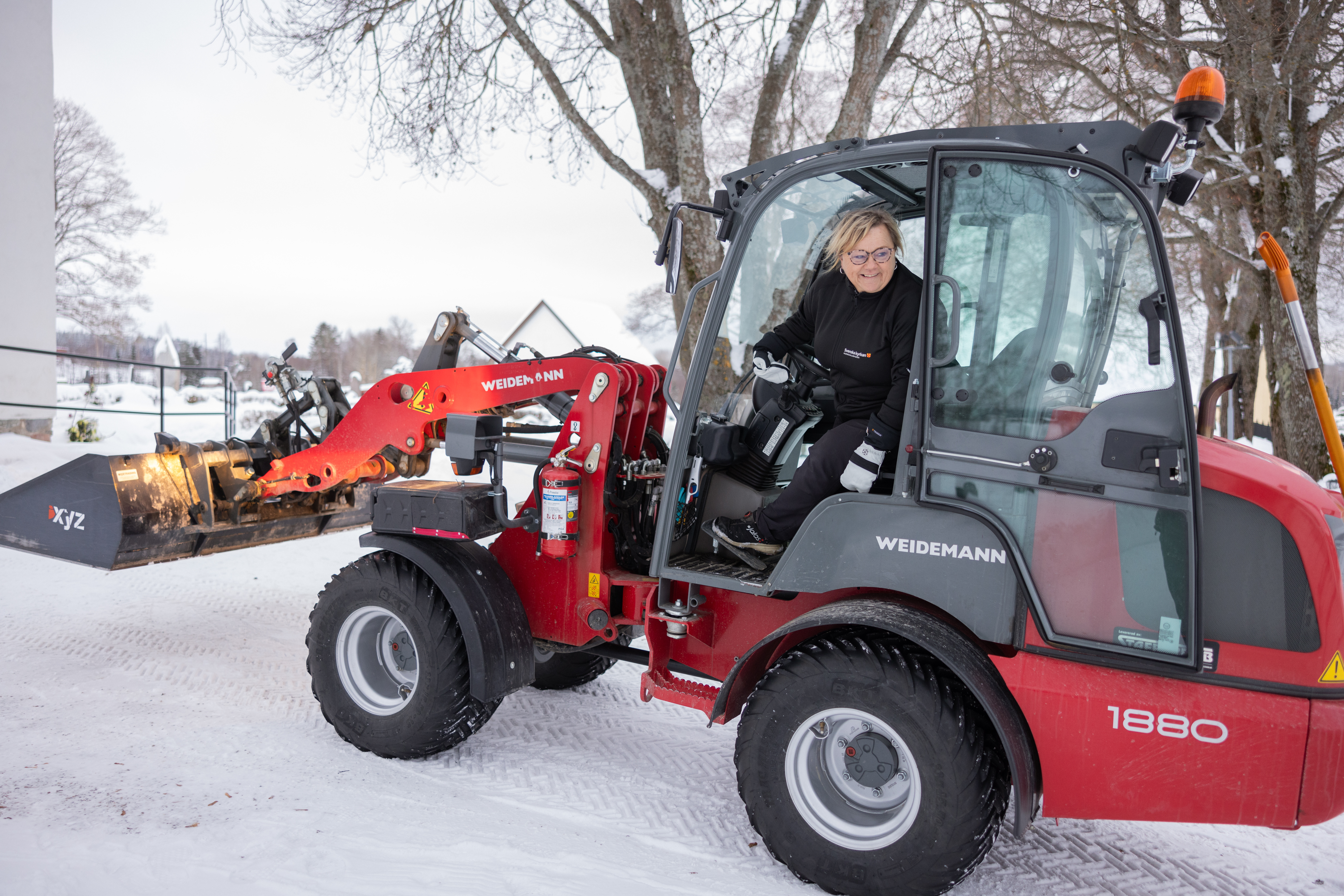 En vaktmästare skottar snö framför kyrkobyggnad.