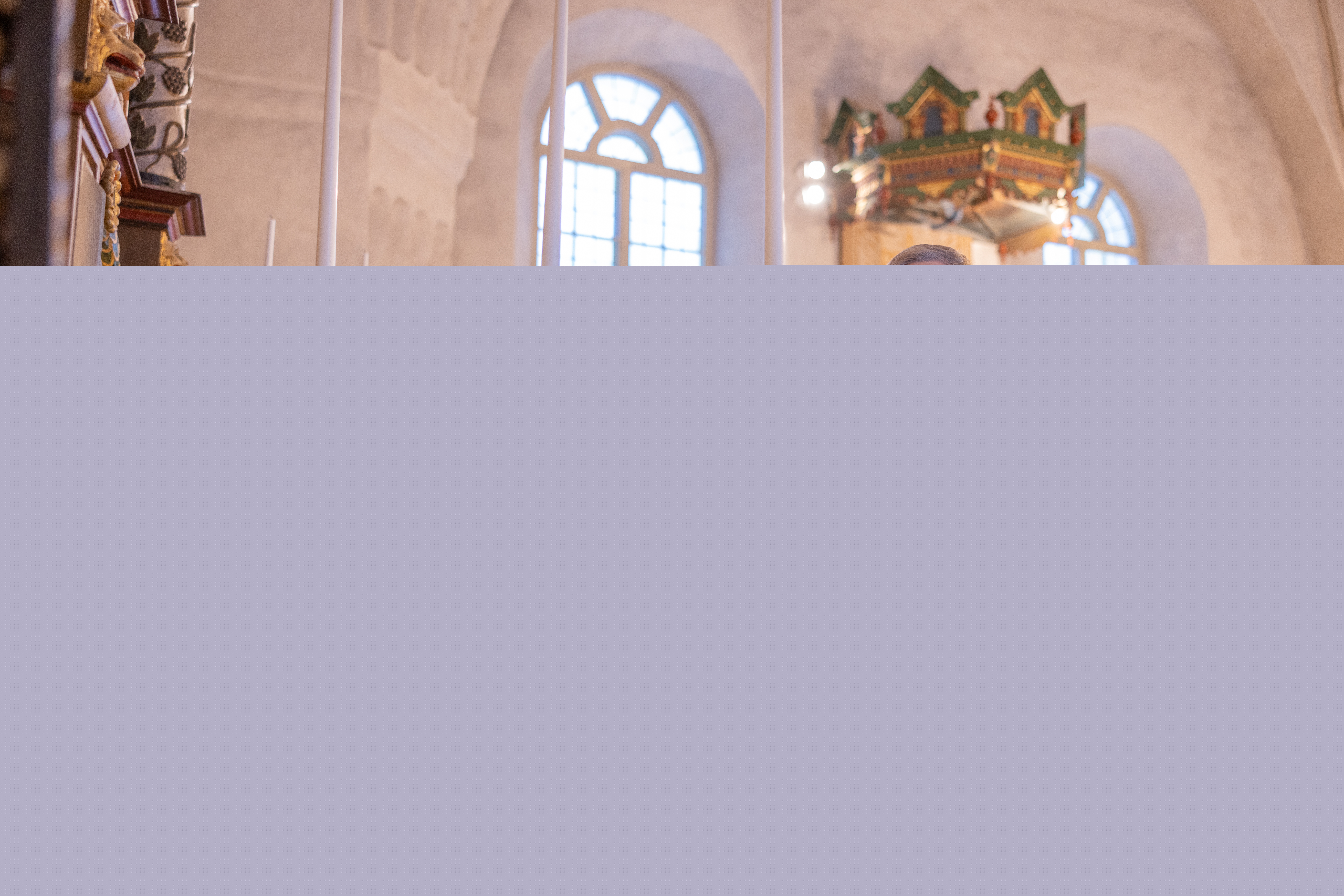 En kyrkvaktmästare sätter långa stearin ljus i de gyllene ljusstakarna på kyrkans altare.