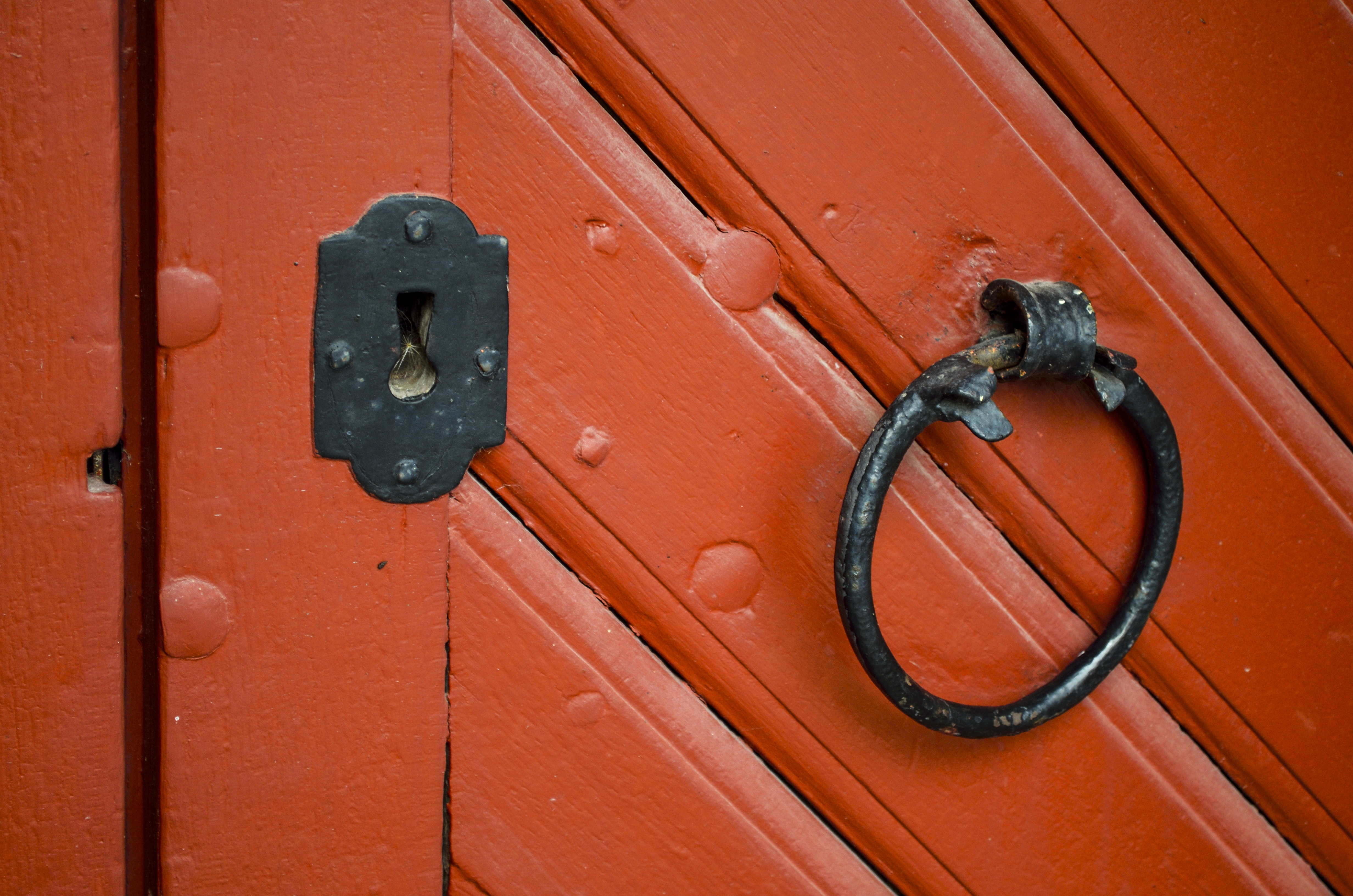 Ett runt dörrhandtag och ett nyckelhål i svart smide på en röd trädörr.