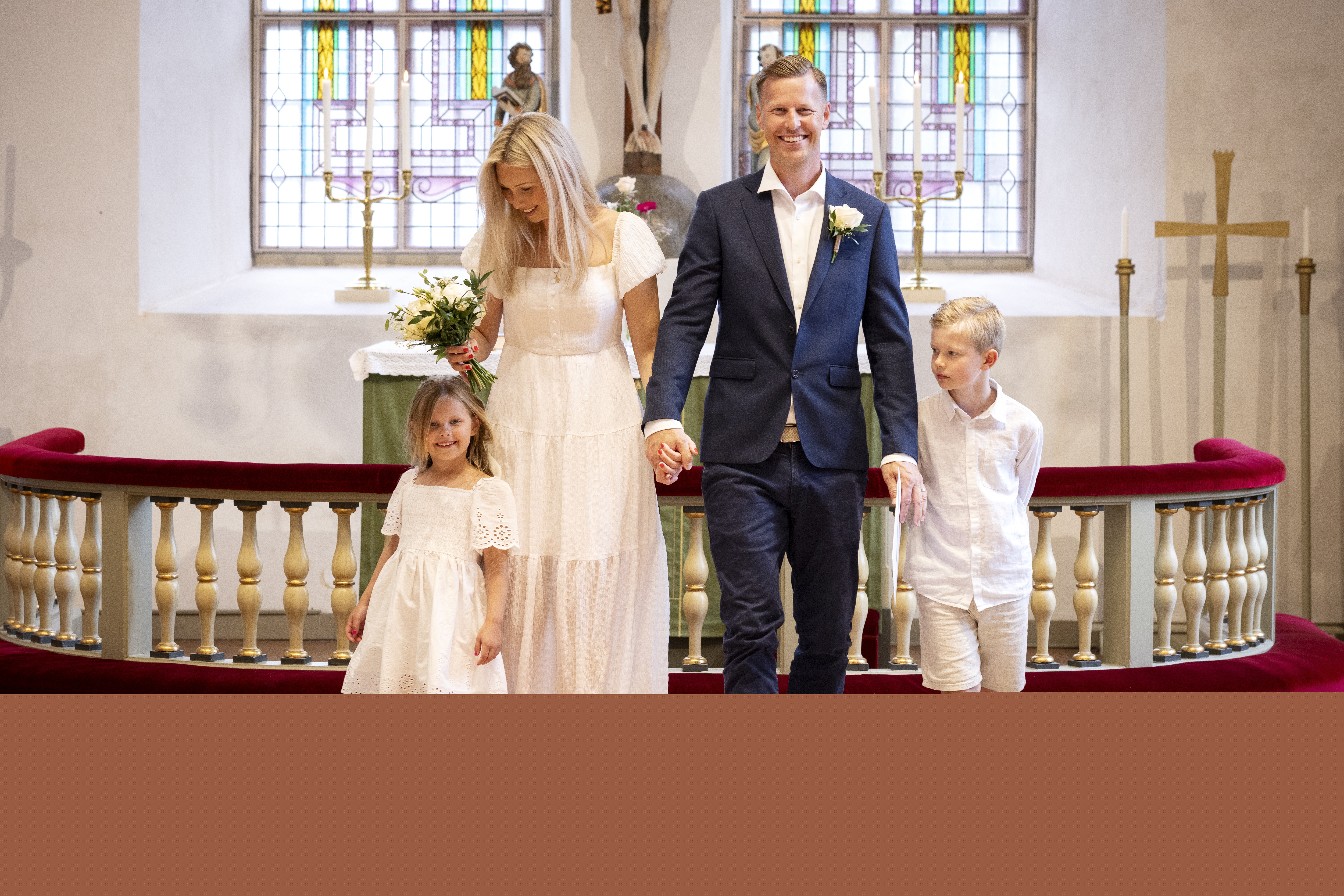 Drop-in vigsel i en kyrka. Ett brudpar står framför altarringen. Två ljusklädda barn står bredvid.