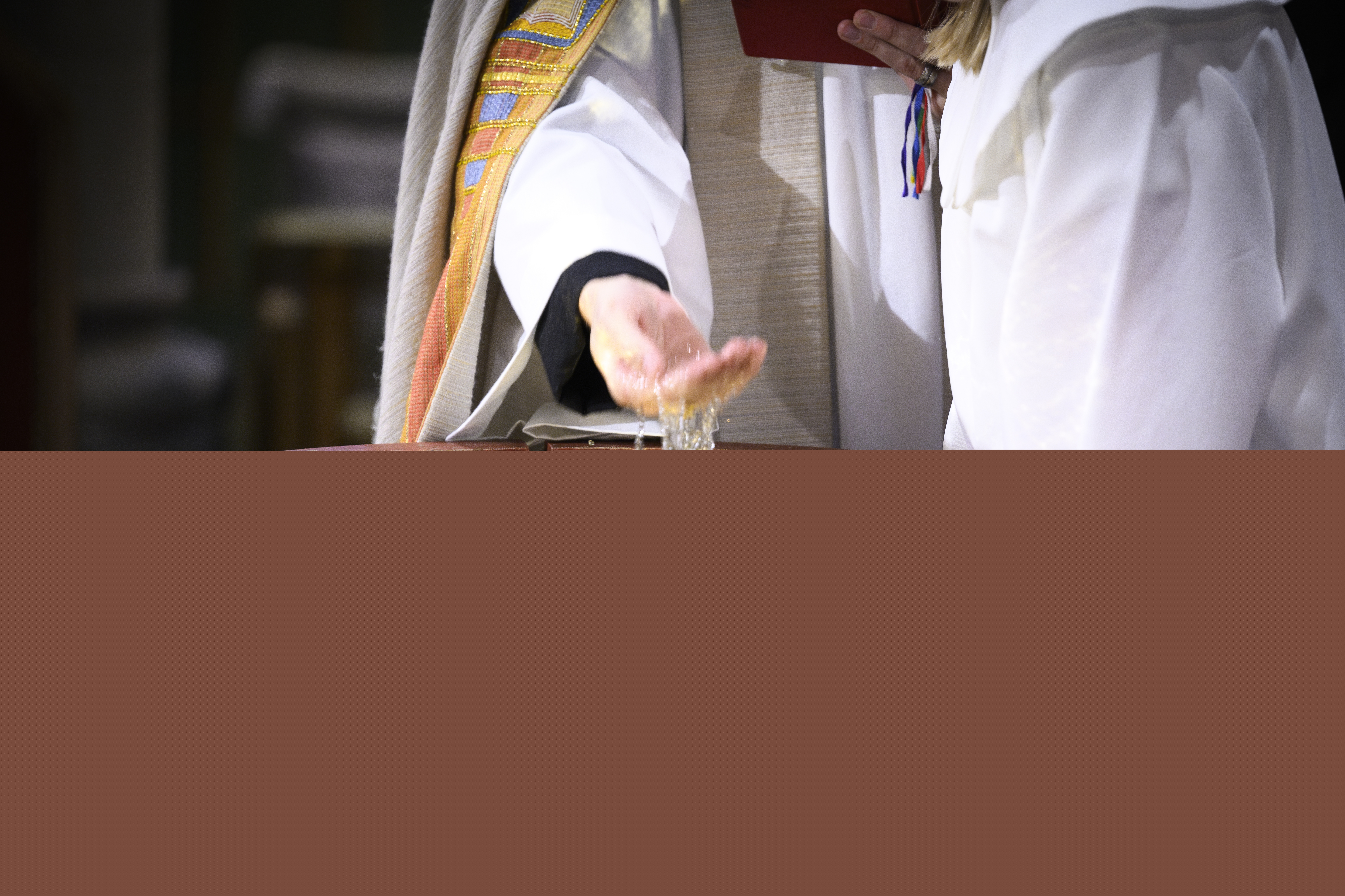 En präst står vid en dopfunt och kupar sin hand i vattnet.