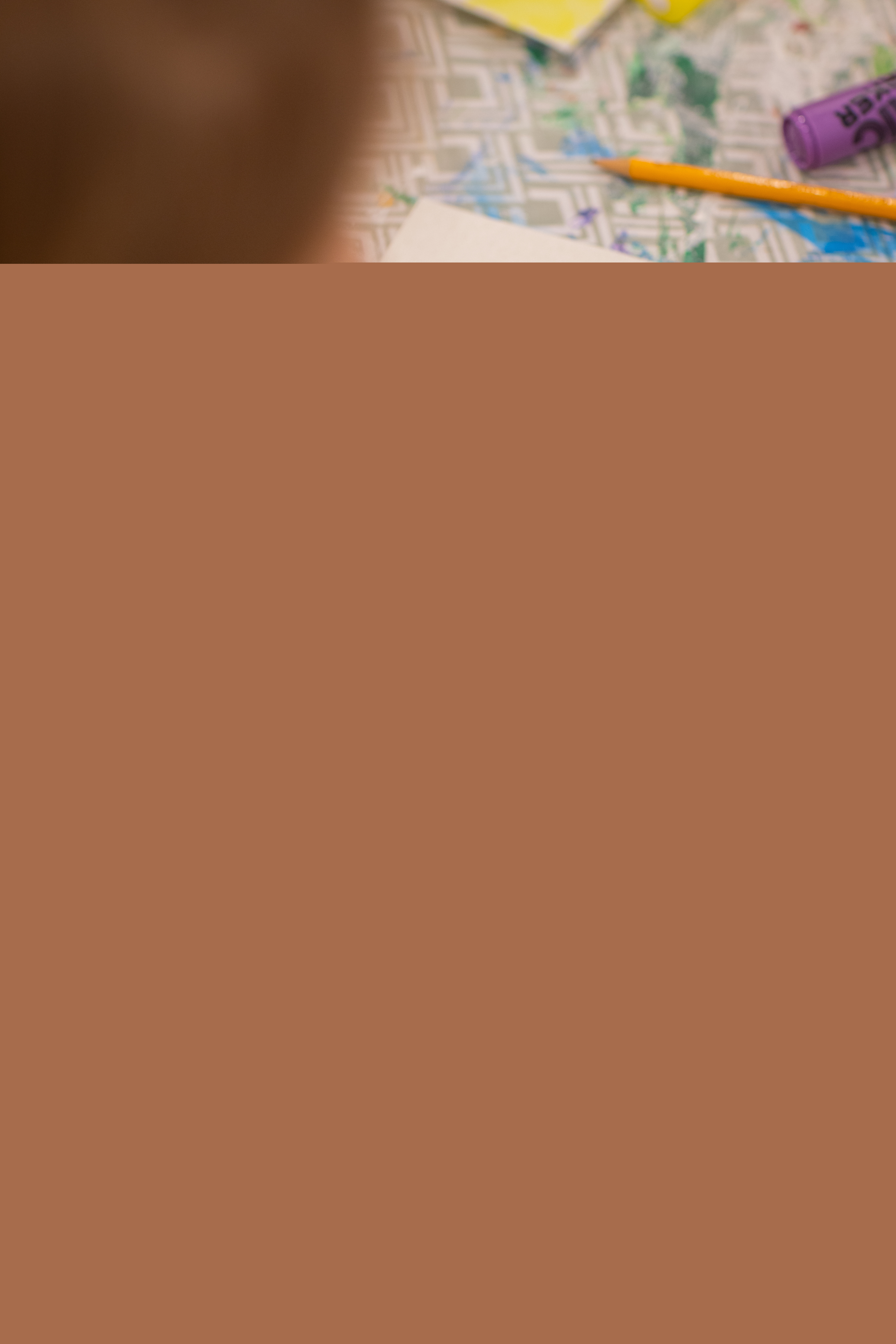 En person sitter vid ett bord och målar ett rött hjärta med målarpensel.