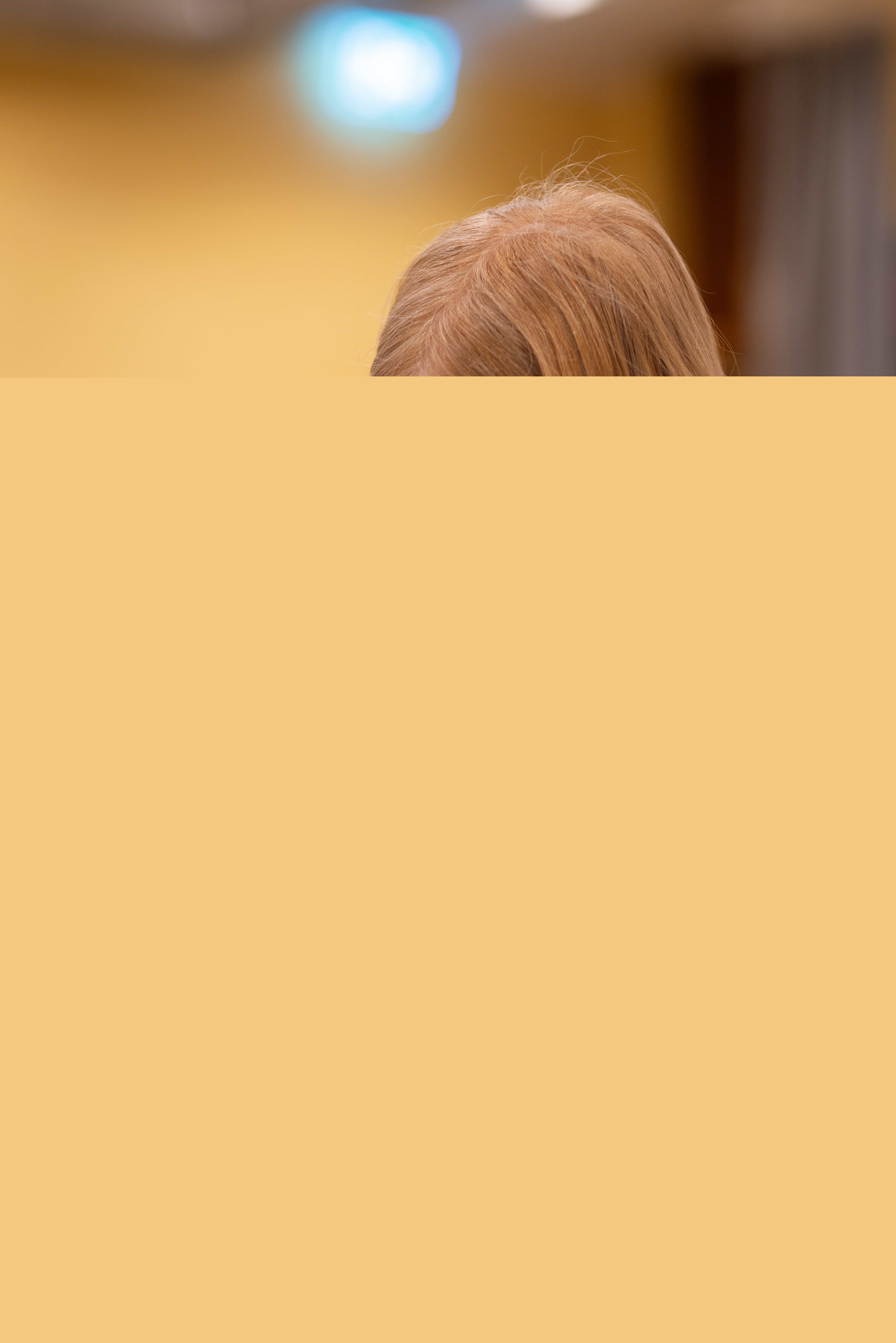 En rödhårig flicka sitter vid ett bord och målar med pensel.