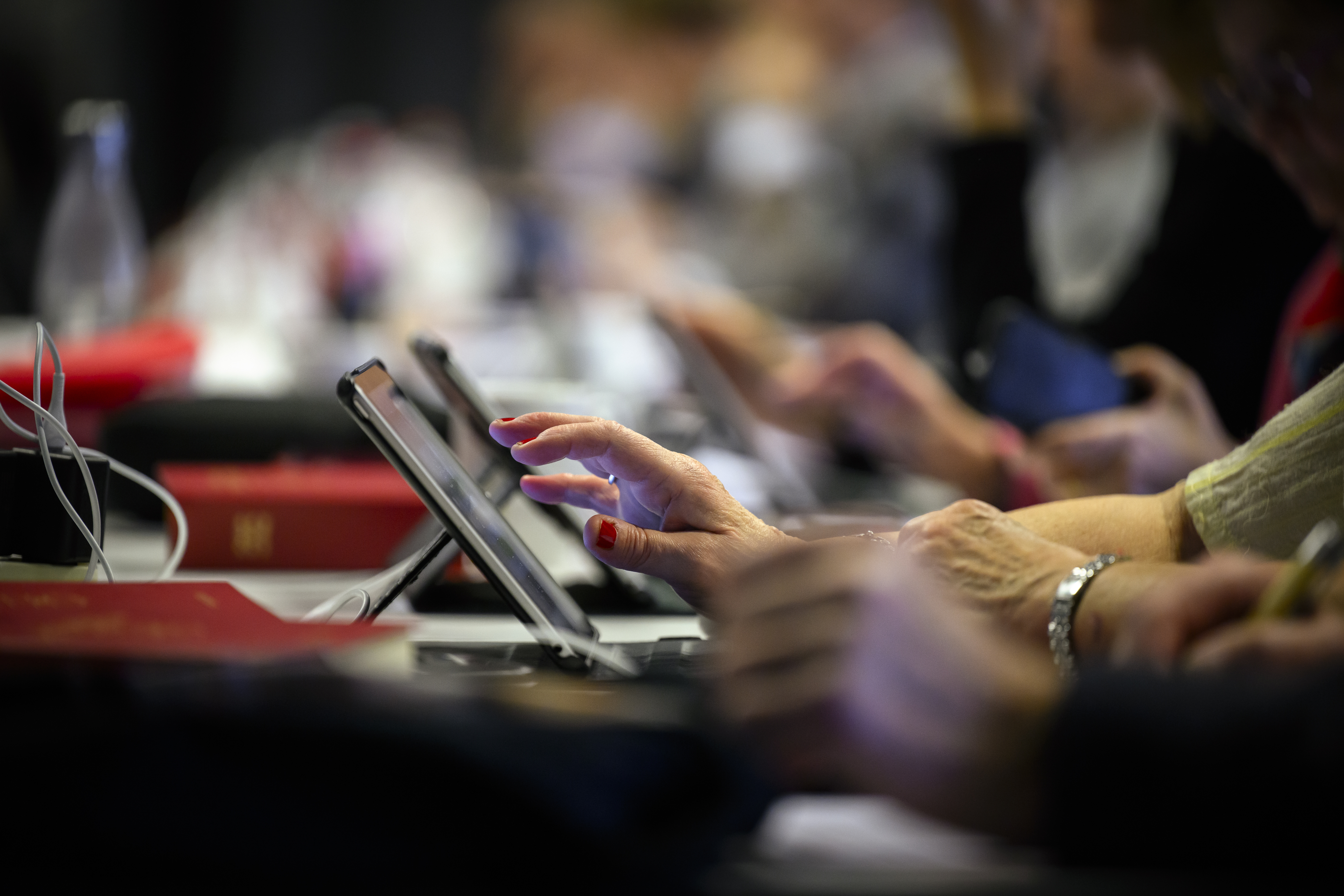 Personer sitter framför sina läsplattor. Psalmböcker ligger på bordet.