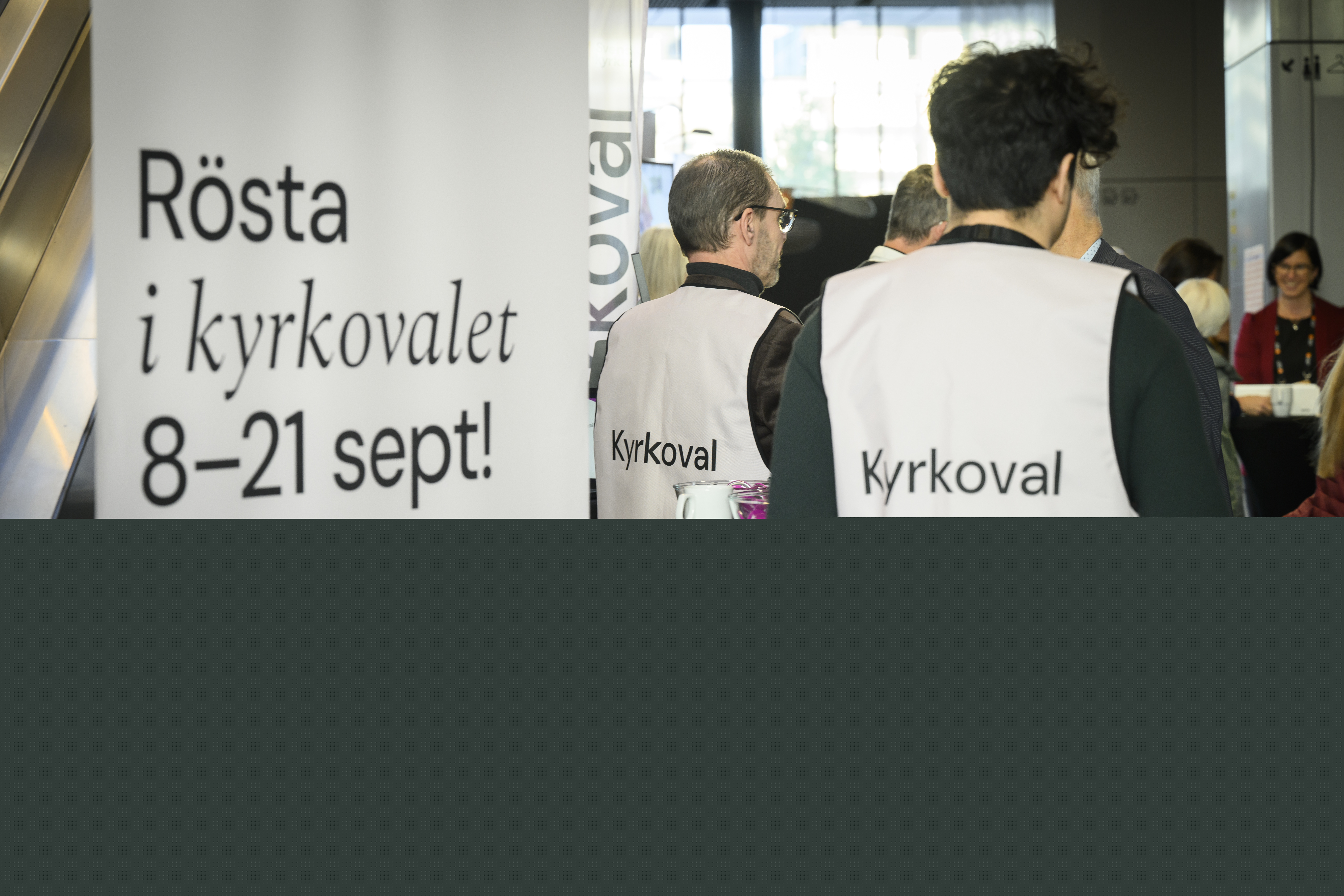 En man i väst med texten Kyrkoval står vid en roll-up med texten Rösta i kyrkovalet 8-21 september.