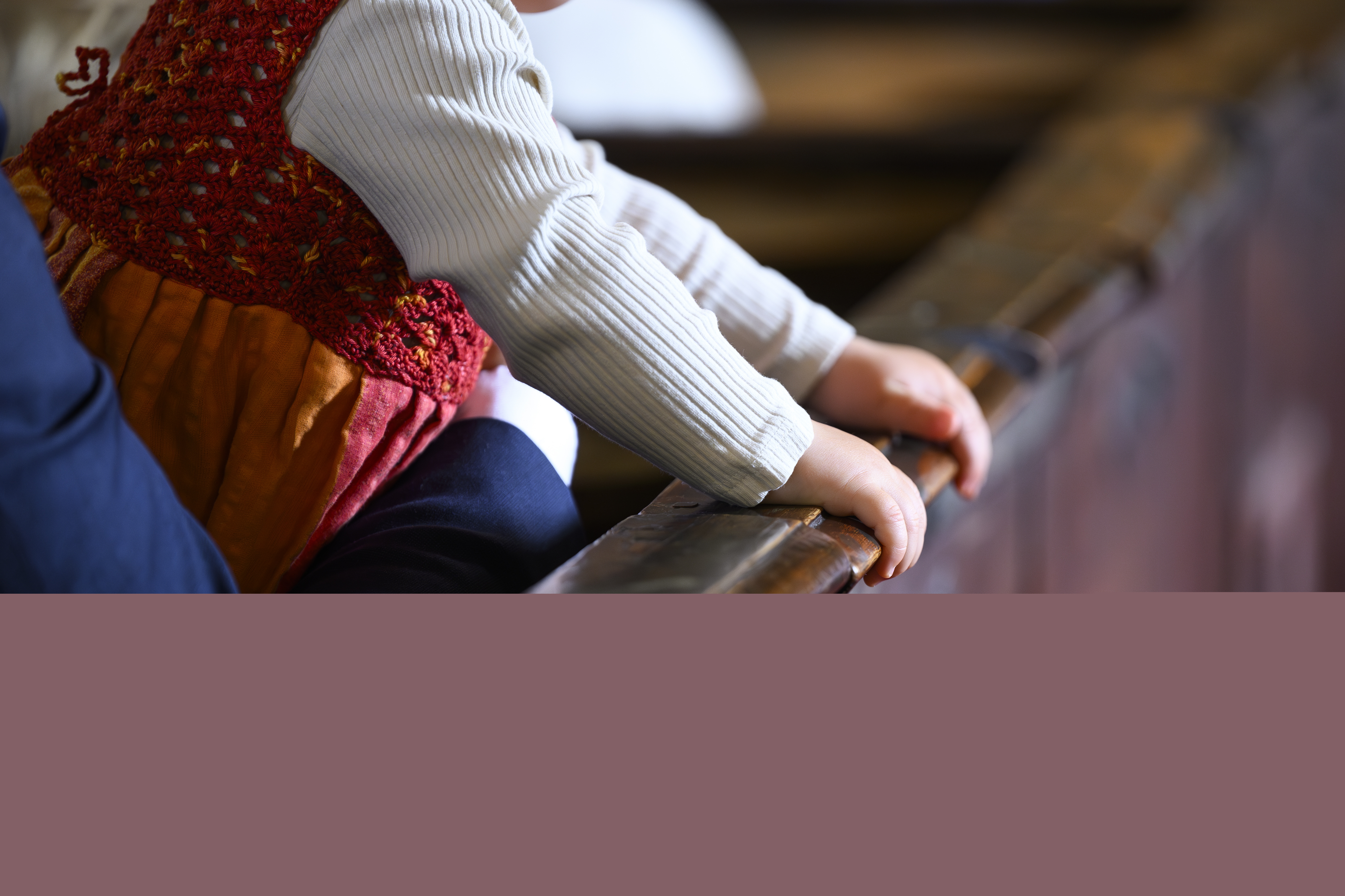 Ett litet barn är i famnen på en person som sitter i kyrkbänken. Barnet håller sina händer på kyrkbänksdörren.