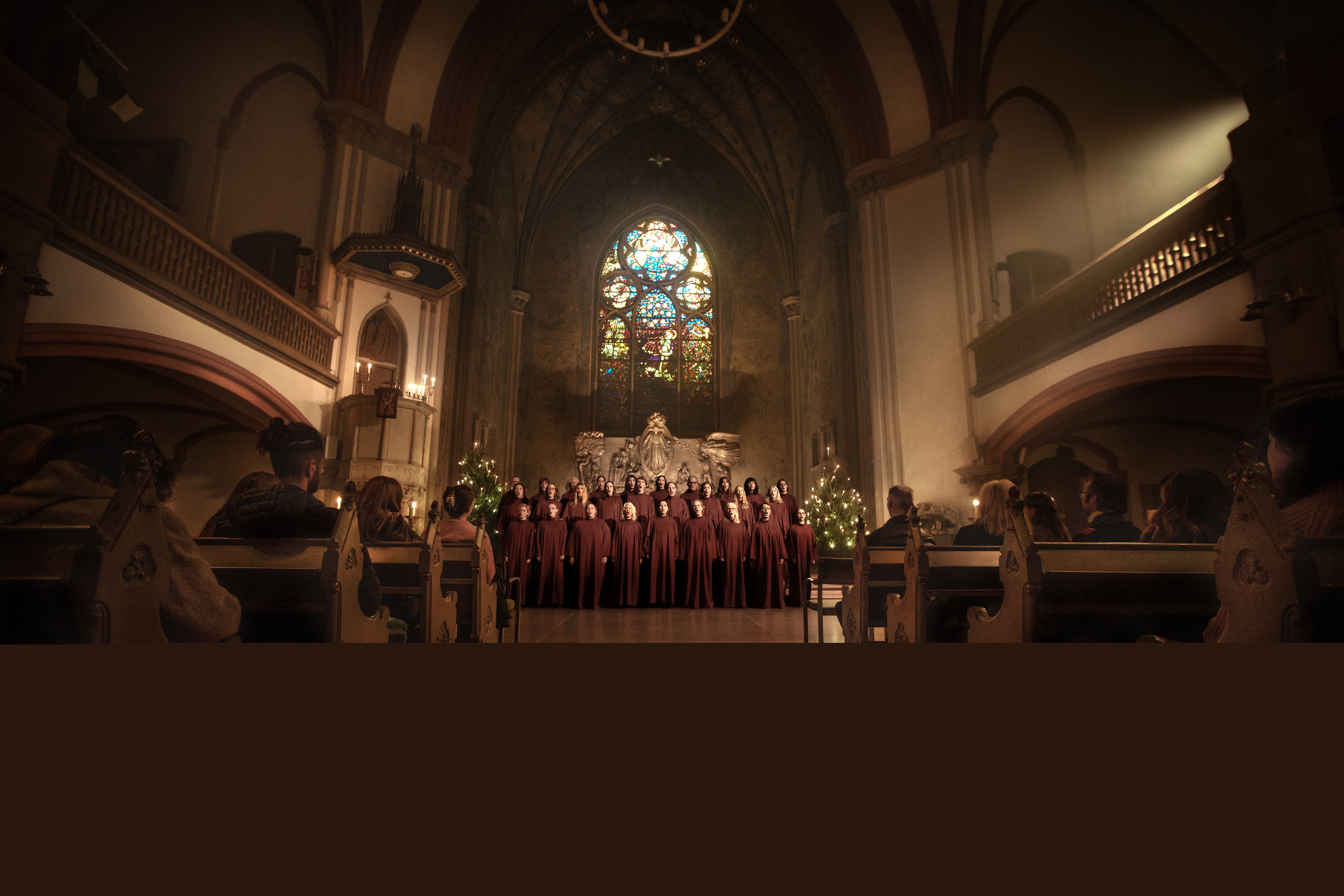 En altargång med kyrkbänkar och två upplysta ljuskronor på varsin sida. En kör står i koret.