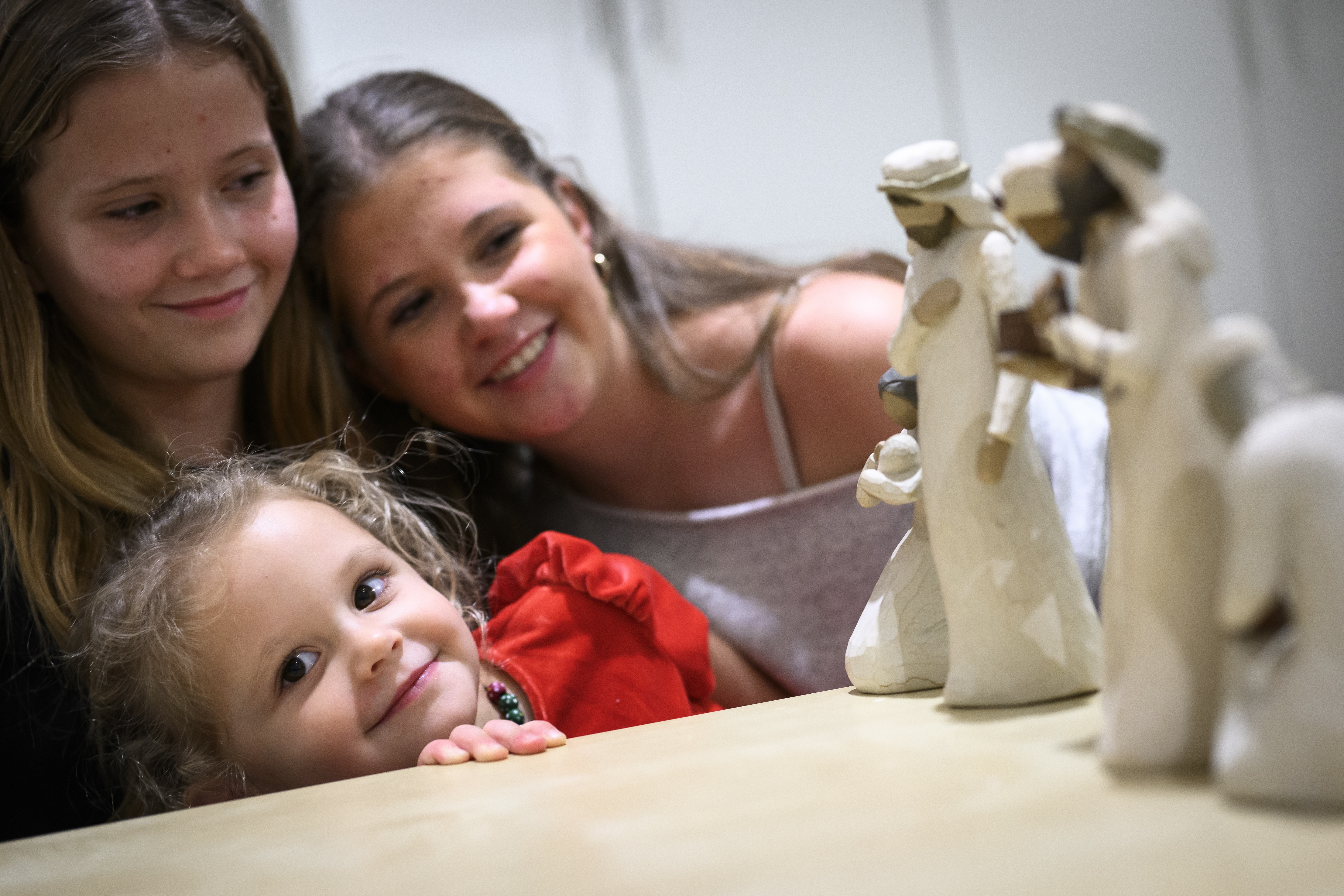 Tre leende flickor sitter tillsammans vid ett bord. Flickorna tittar på trädockor som föreställer dom tre vise männen som står uppställda på bordet.