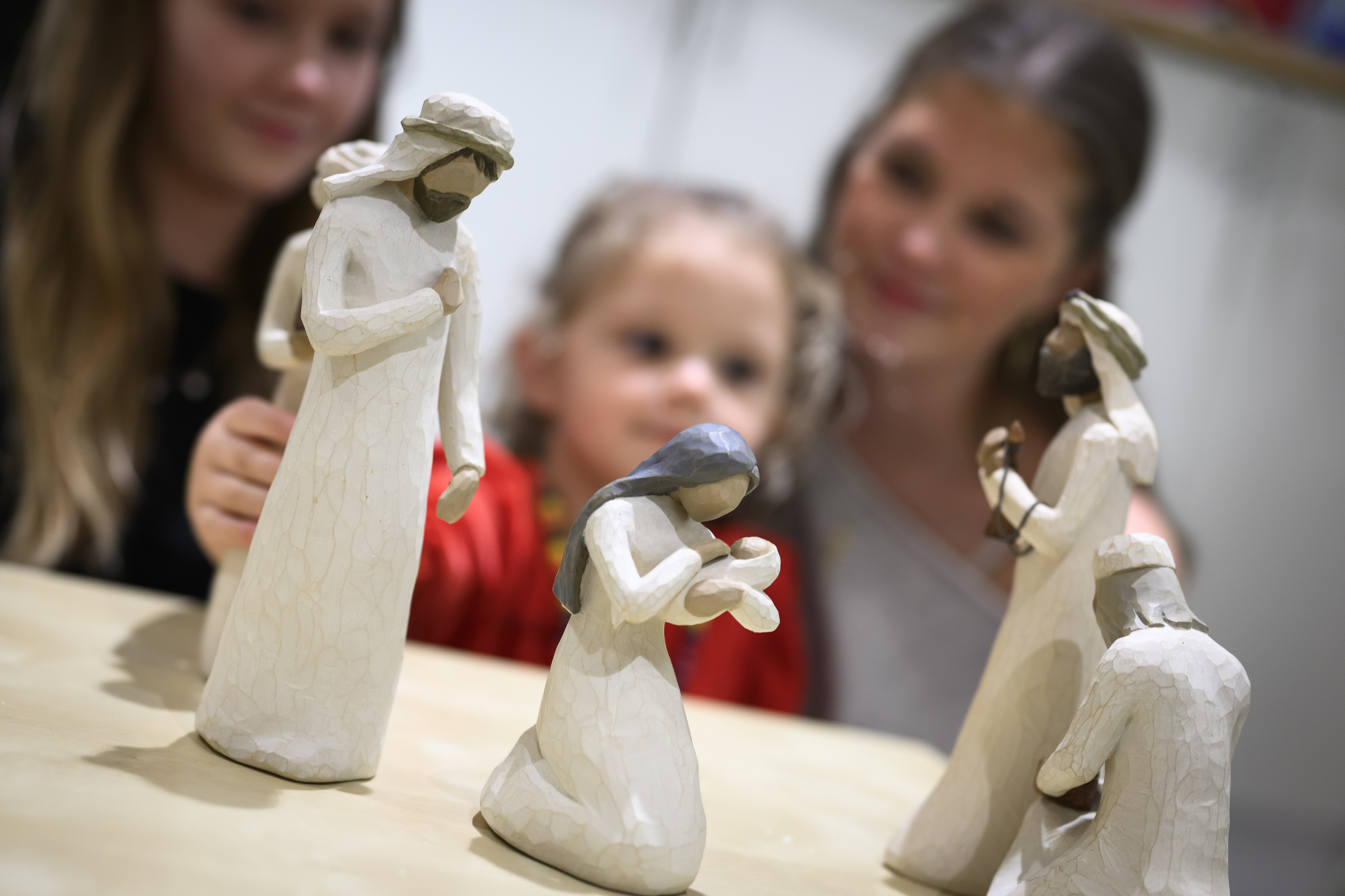 Trädockor som föreställer Jungfru Maria med Jesusbarnet i famnen och de tre vise männen, står på ett bord. Ett barn och två ungdomar sitter runt bordet.