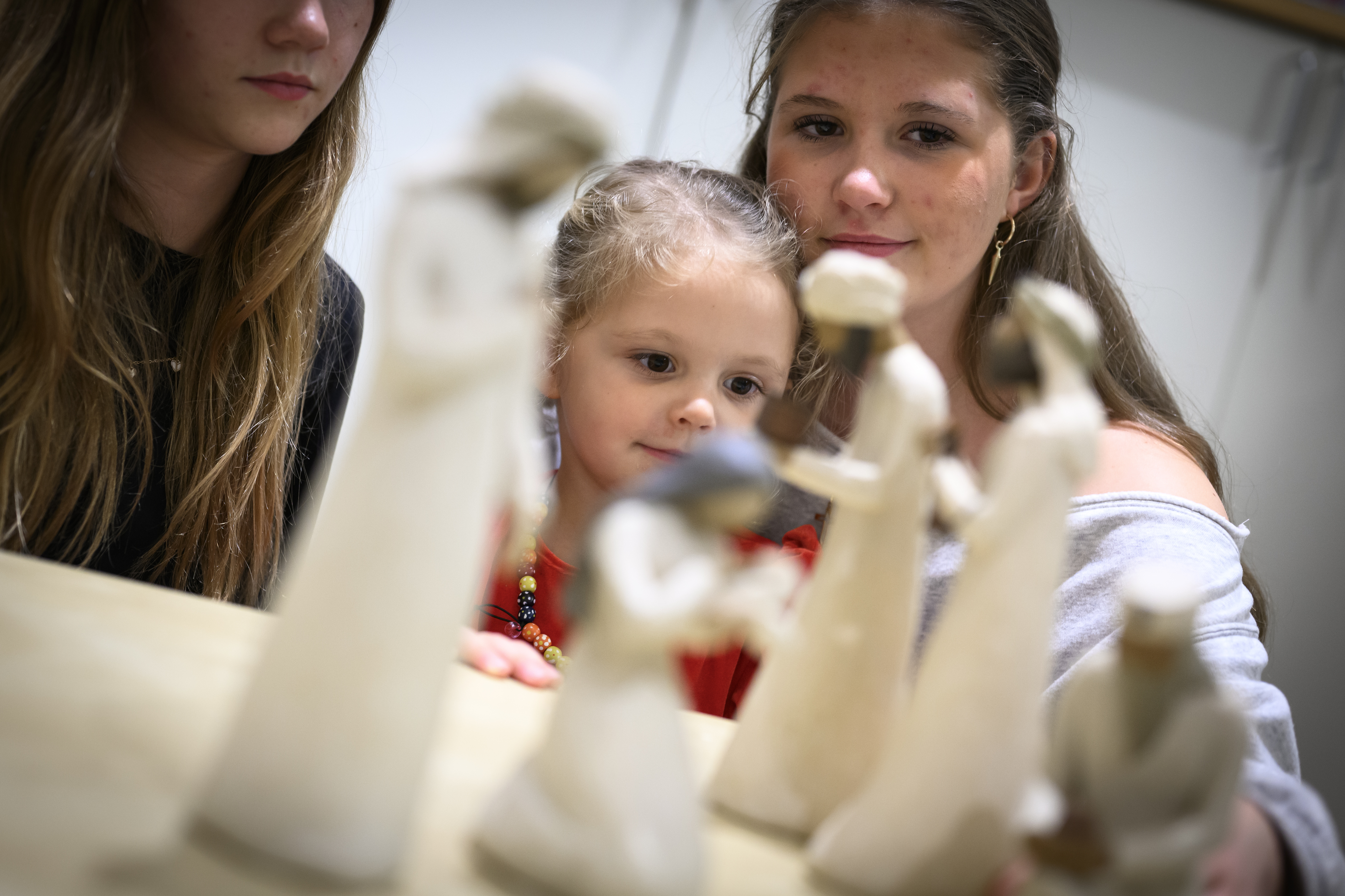 Trädockor som föreställer Jungfru Maria med Jesus-barnet i famnen och de tre vise männen står på ett bord. Ett barn och två ungdomar sitter runt bordet.
