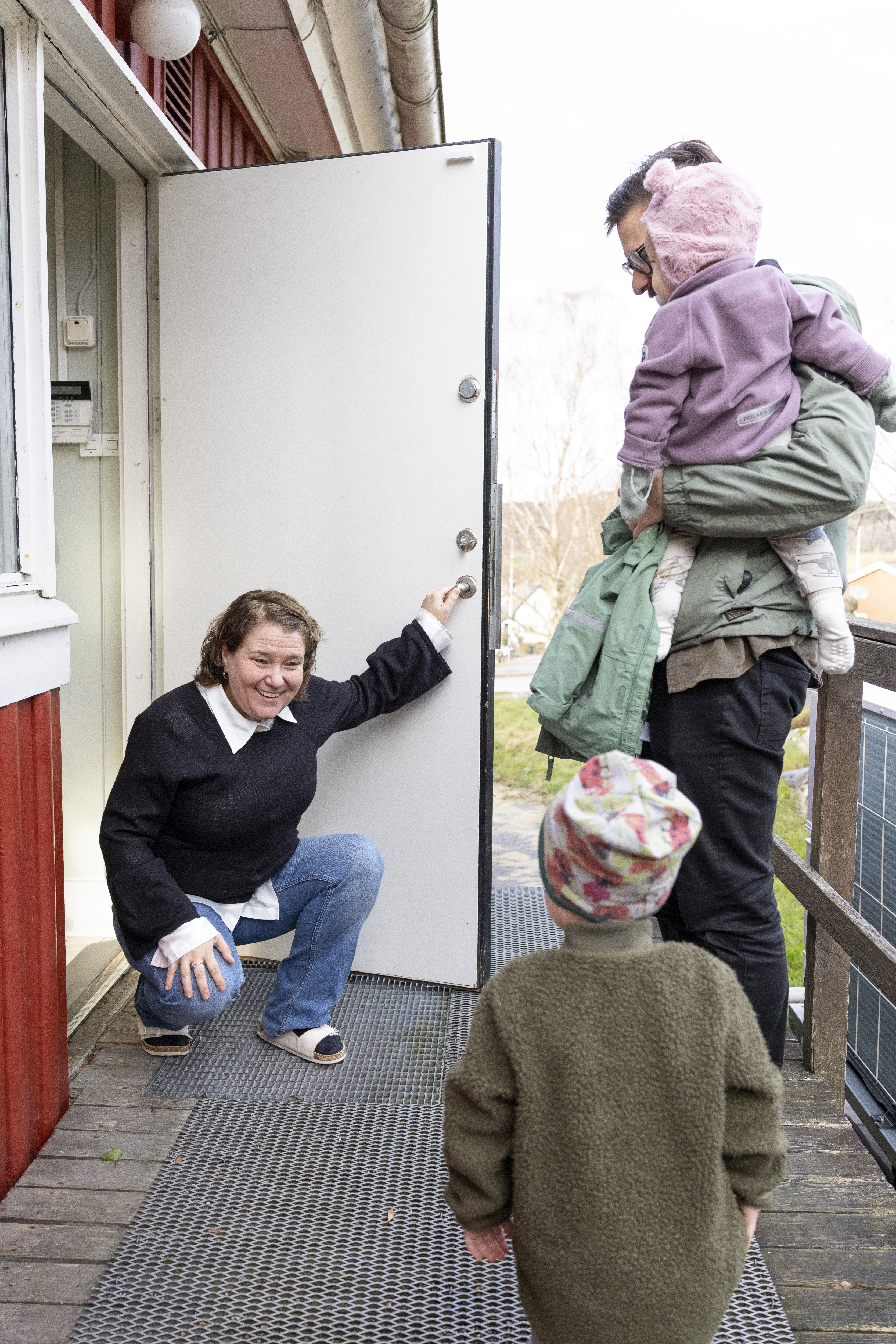 En kvinna sitter på huk utomhus och ler mot ett barn. En man med ett barn i famnen står bredvid.