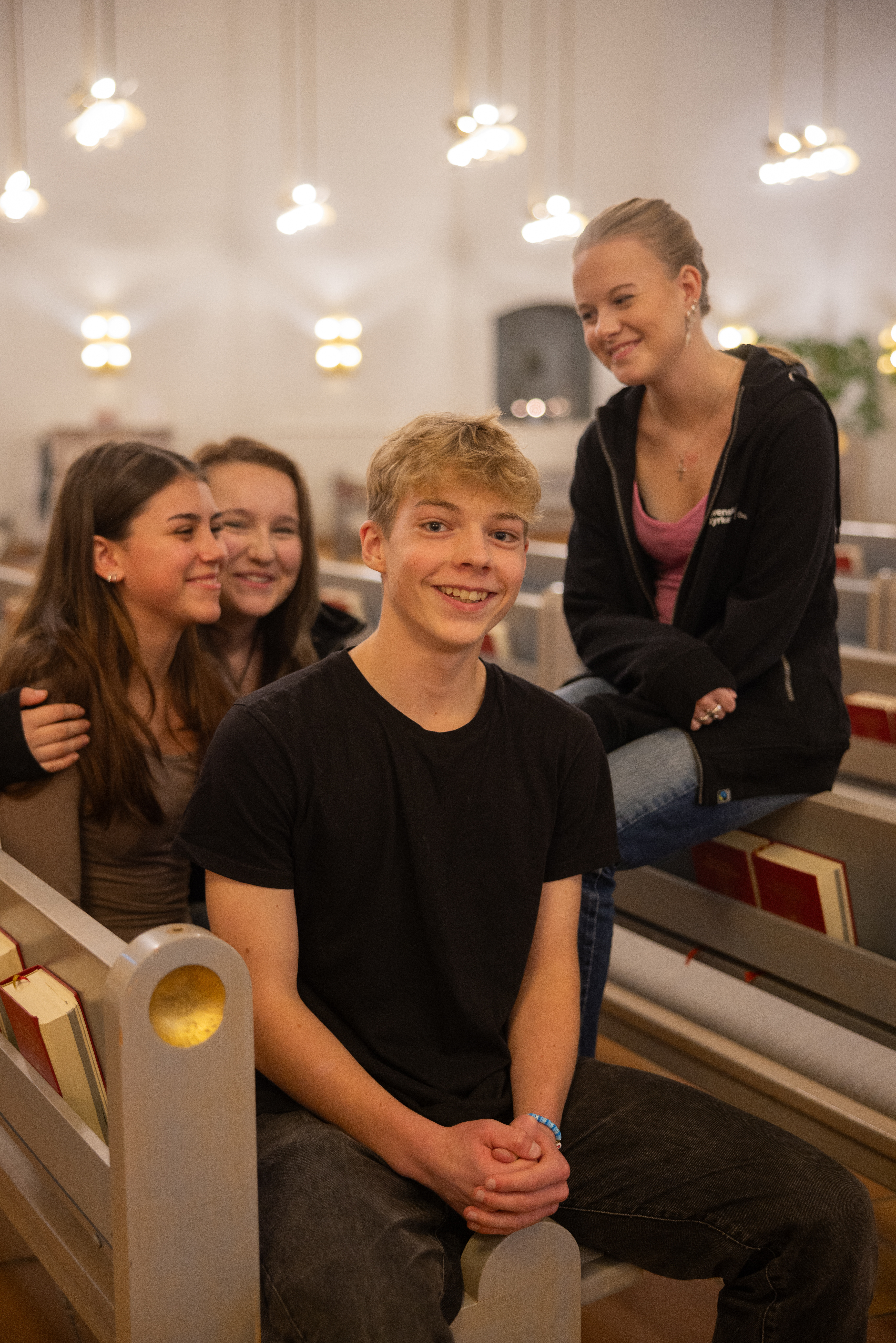 Fyra glada ungdomar sitter i kyrkbänken och tittar in i kameran.