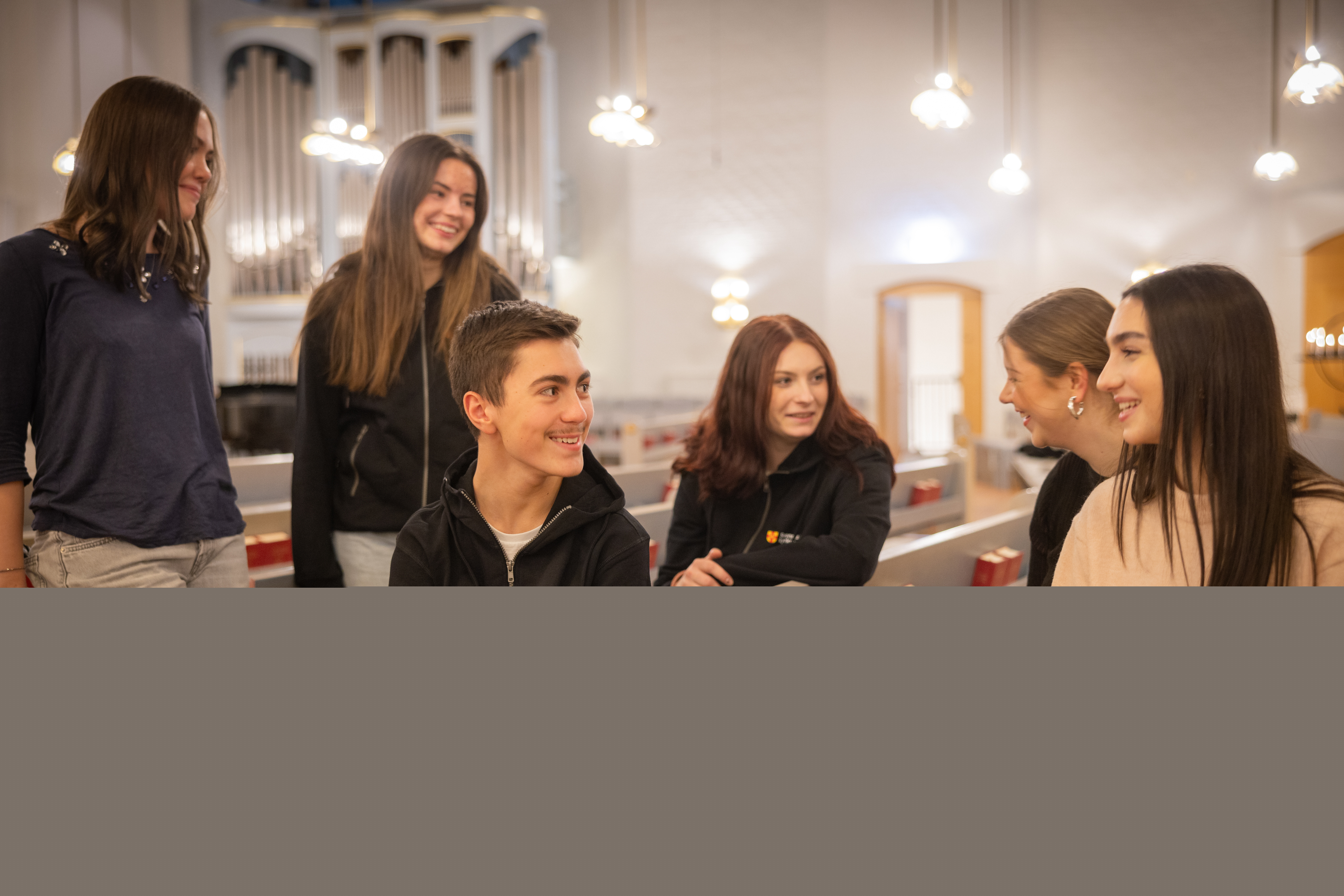 Flera ungdomar samtalar med varandra i en kyrka. Biblar utställda i bänkraderna.