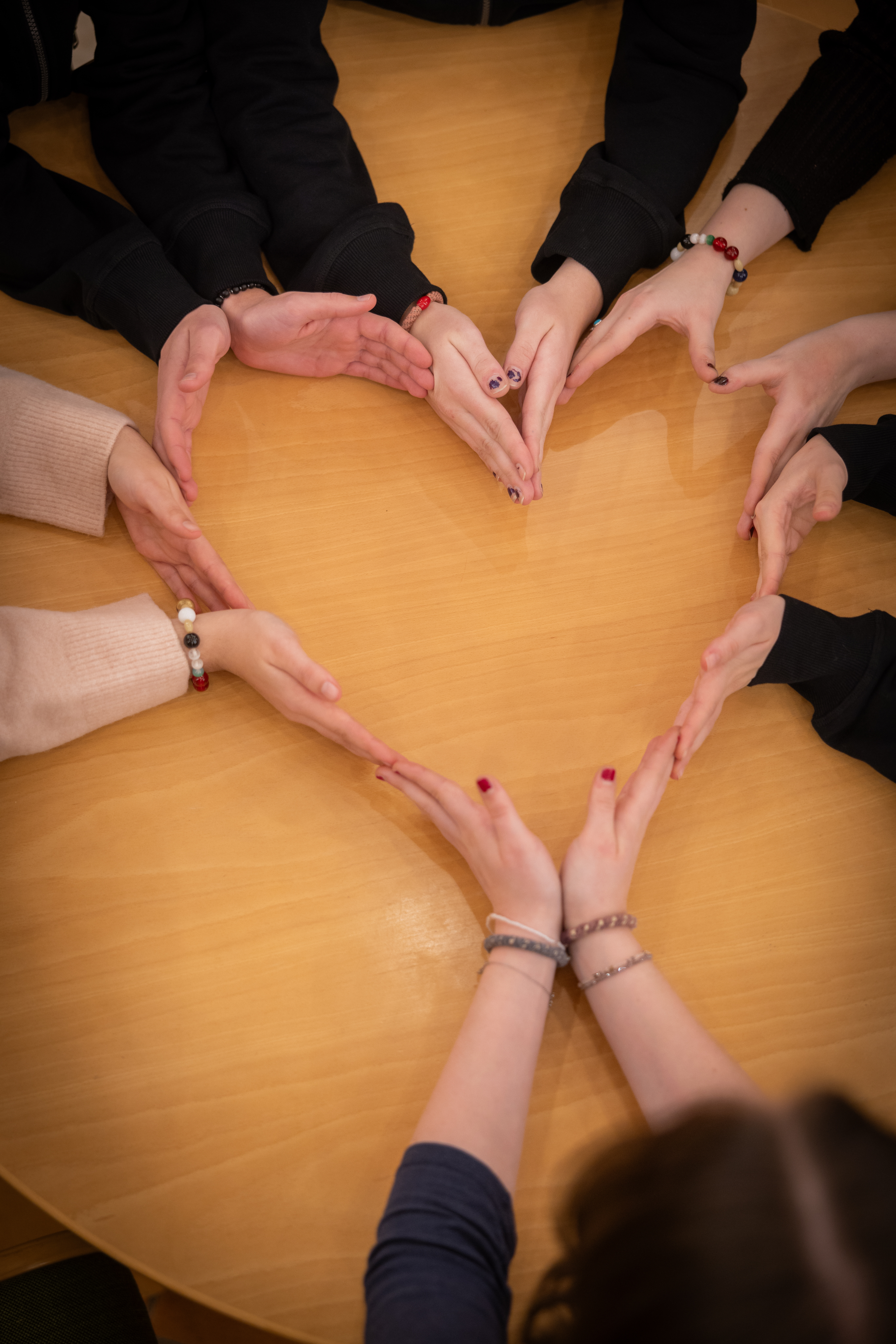 Flera personer sitter vid ett bord och formar  ett hjärta med hjälp av sina händer.
