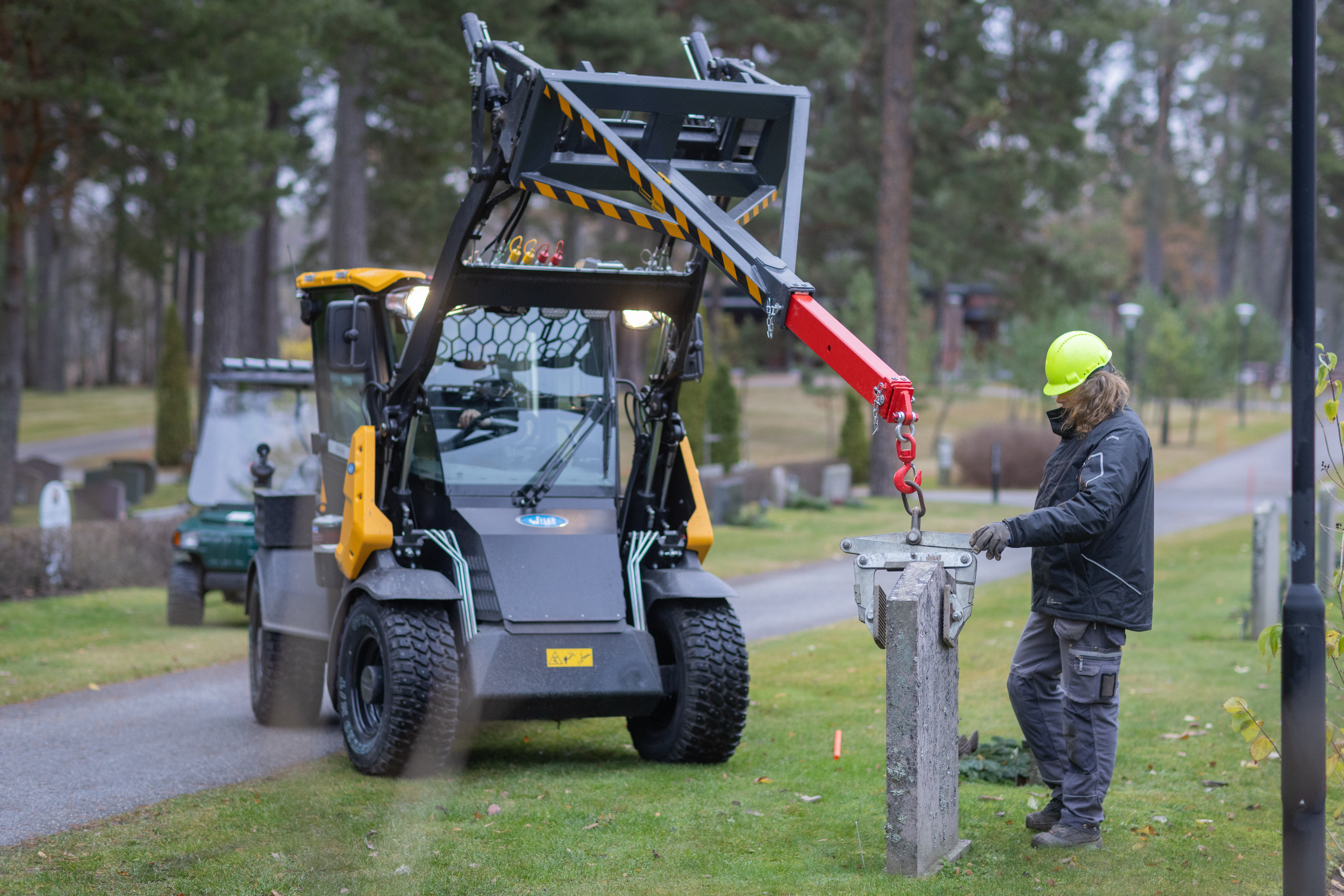 En traktor drar upp en gravsten. Gräs och träd i omgivningen.