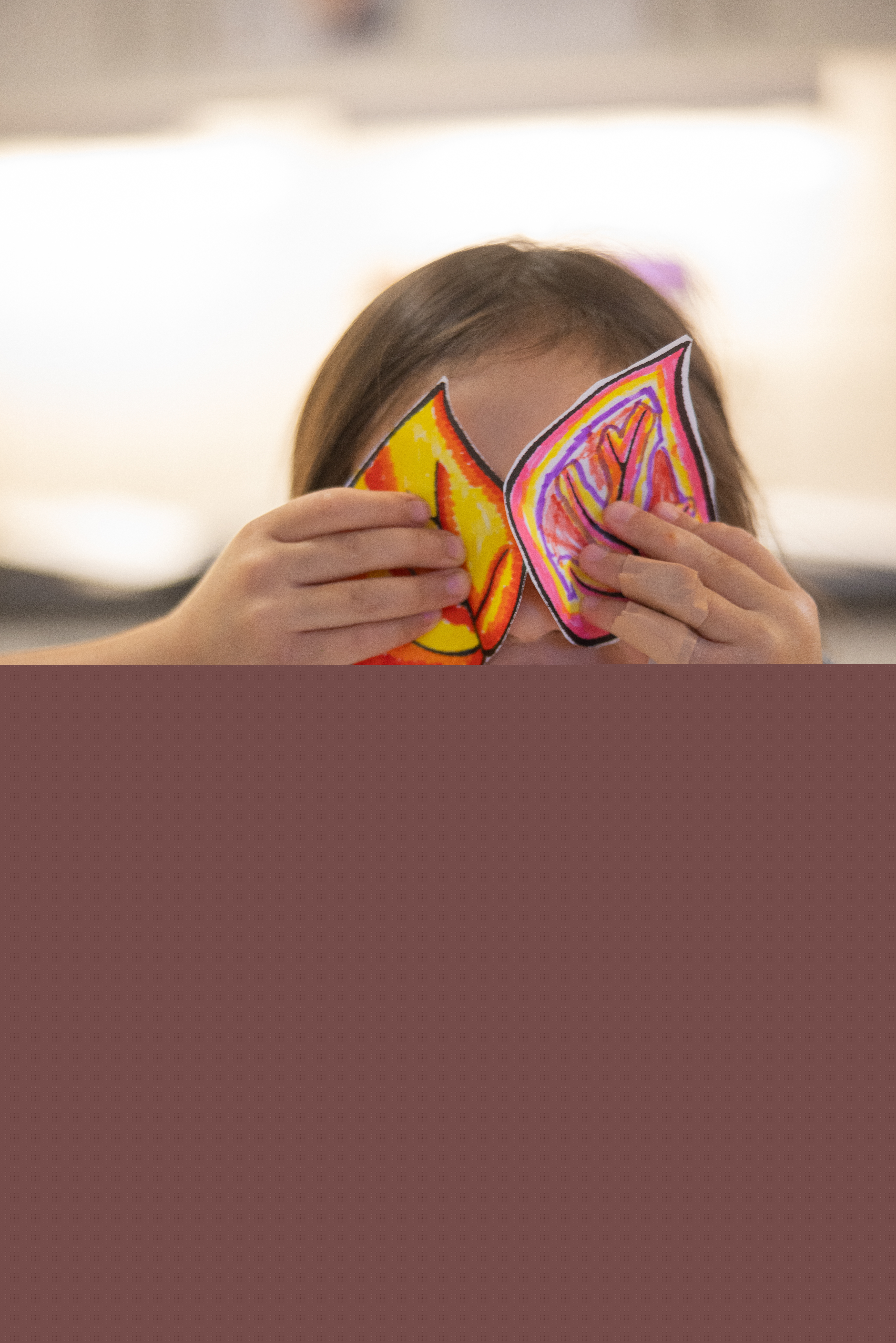 Ett yngre barn med urklippta teckningar av löv framför ögonen.