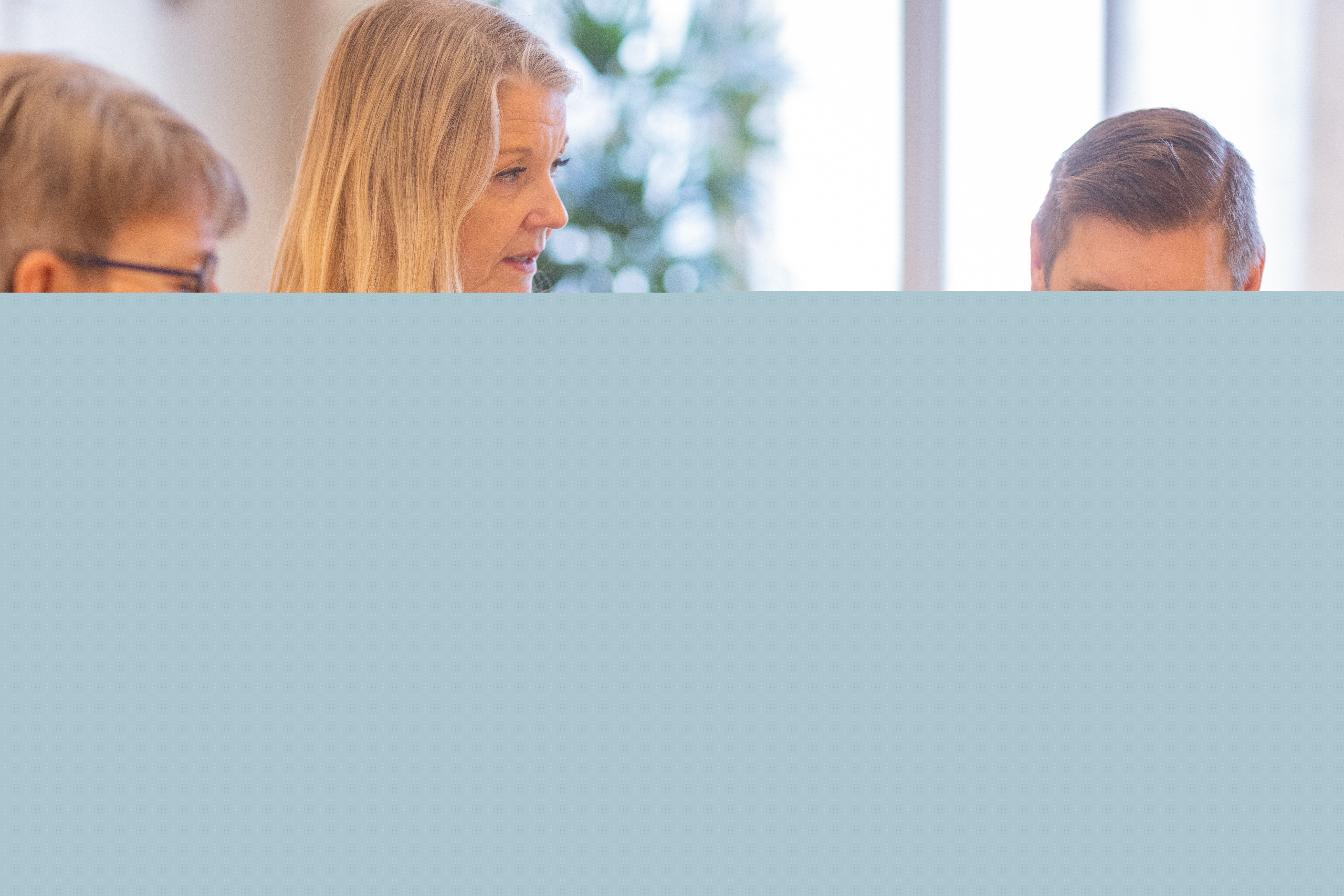 Två kvinnor och en man sitter vid ett bord framför en dator. Oranga blommor och ett värmeljus i förgrunden.