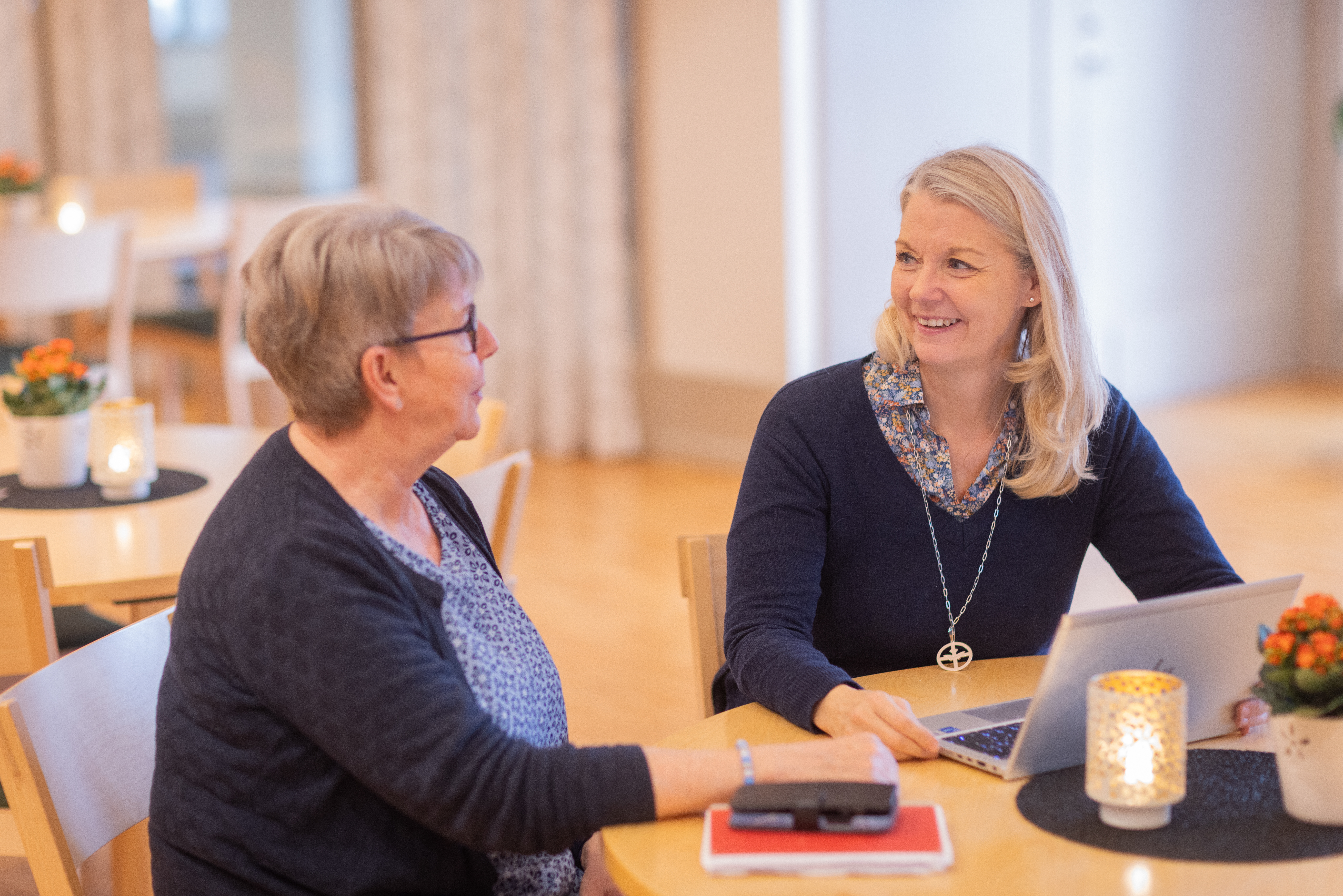 Två kvinnor som sitter vid ett bord har ett trevligt samtal framför en dator.