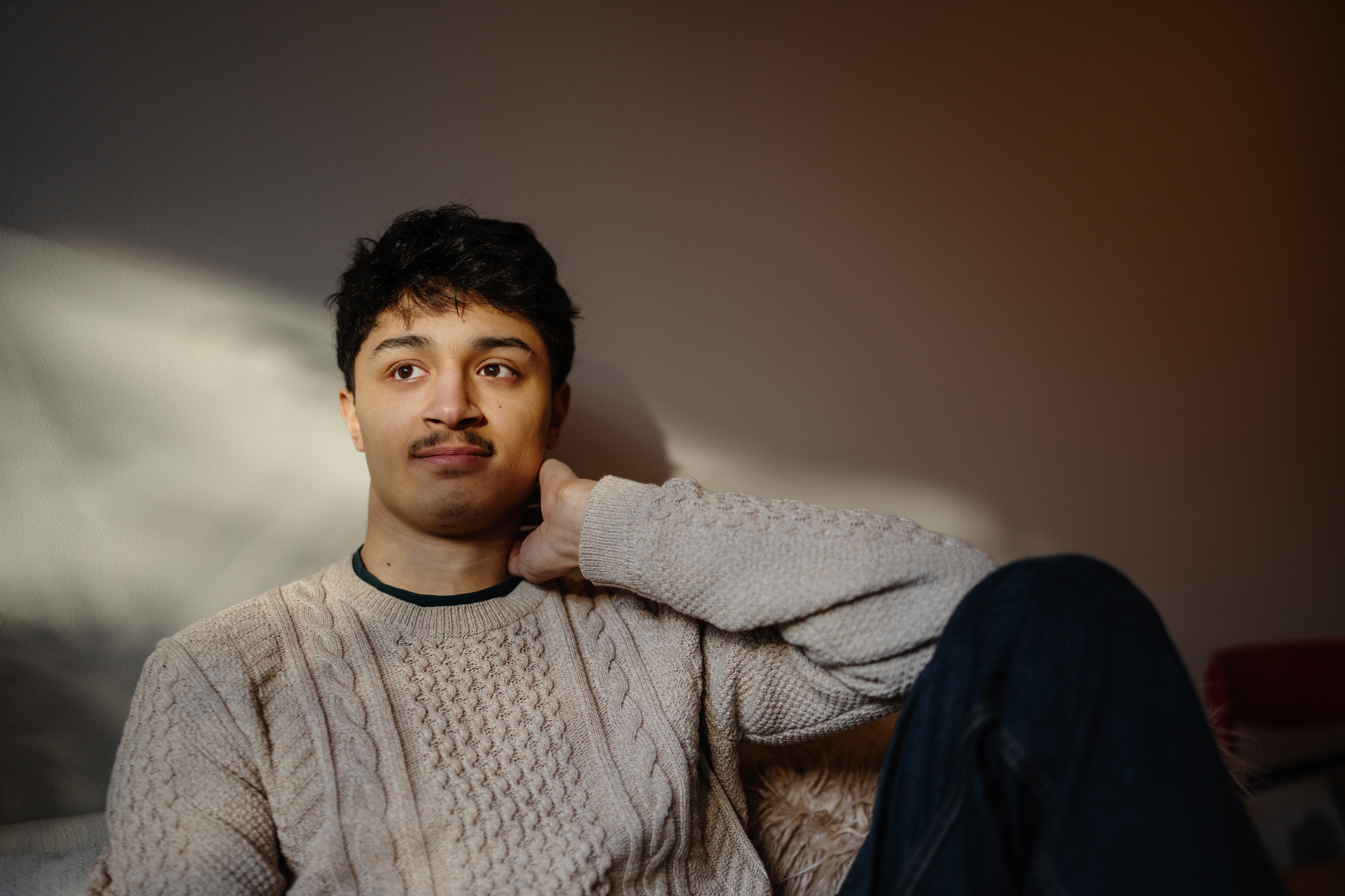 Närbild på en ung man som sitter i en soffa. En strimma solljus syns på väggen i bakgrunden.