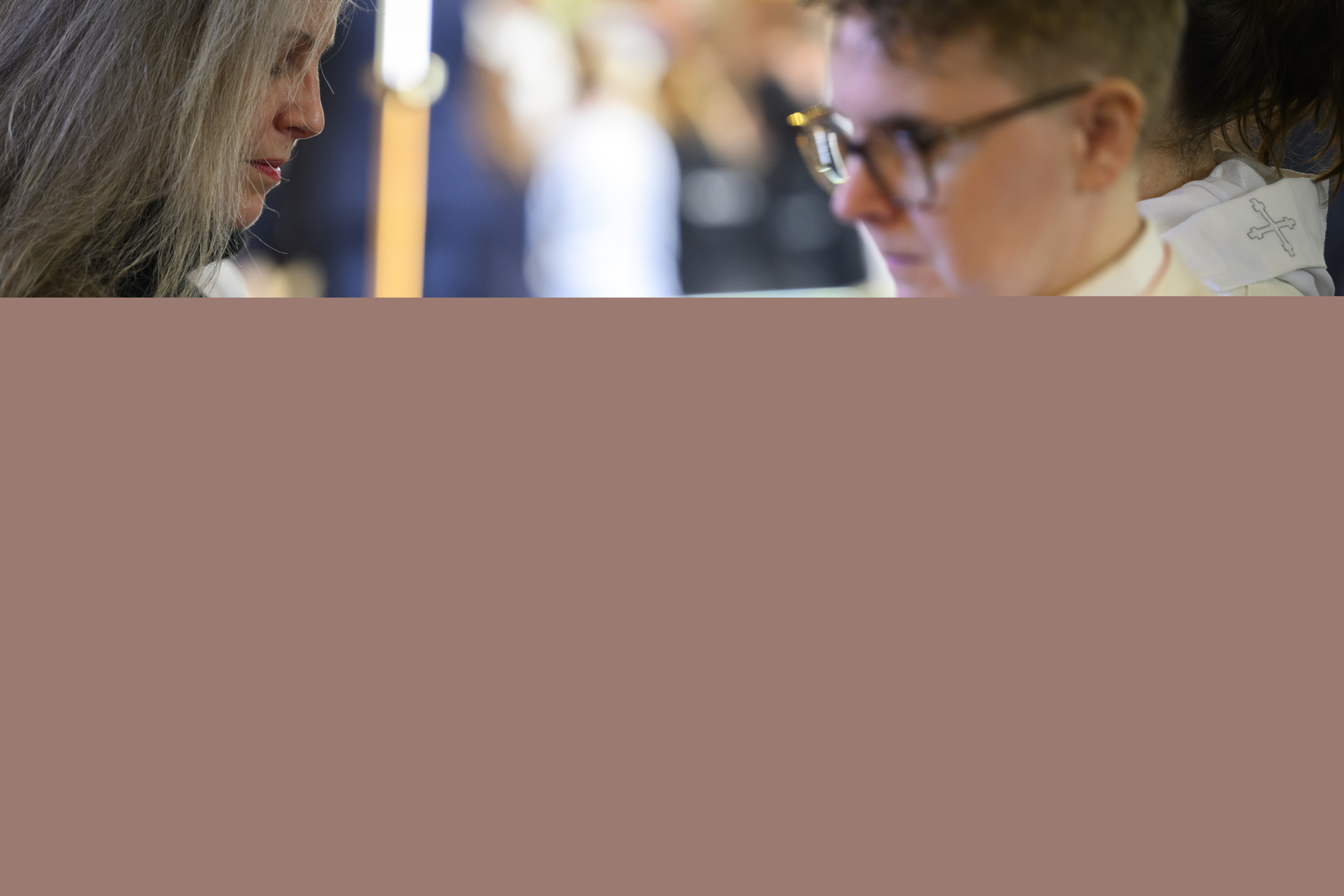 En kvinna i svarta kläder håller en oblat i sin ena hand. Prästen räcker fram kalken.