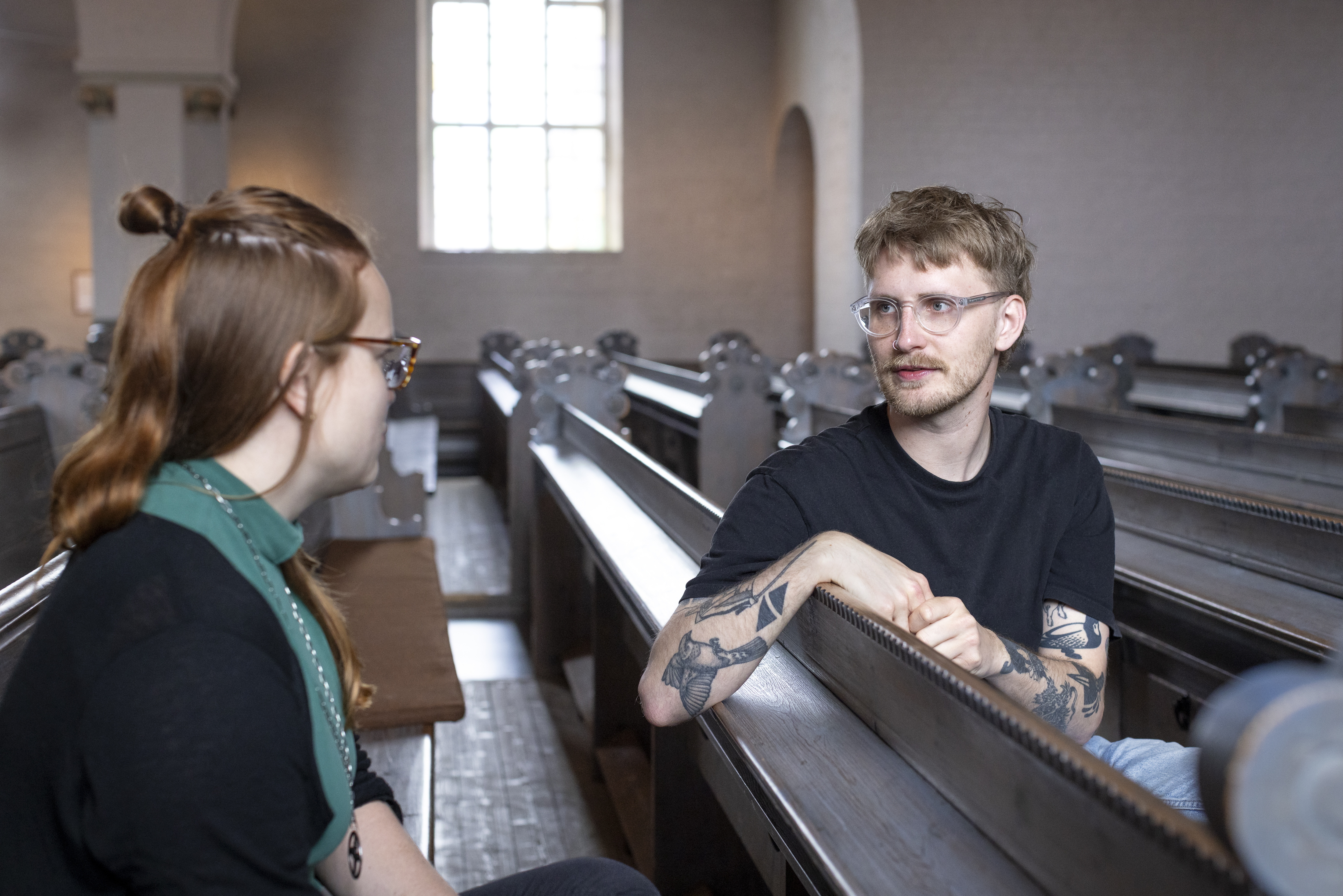 Två personer sitter i en kyrkbänk och pratar med varandra