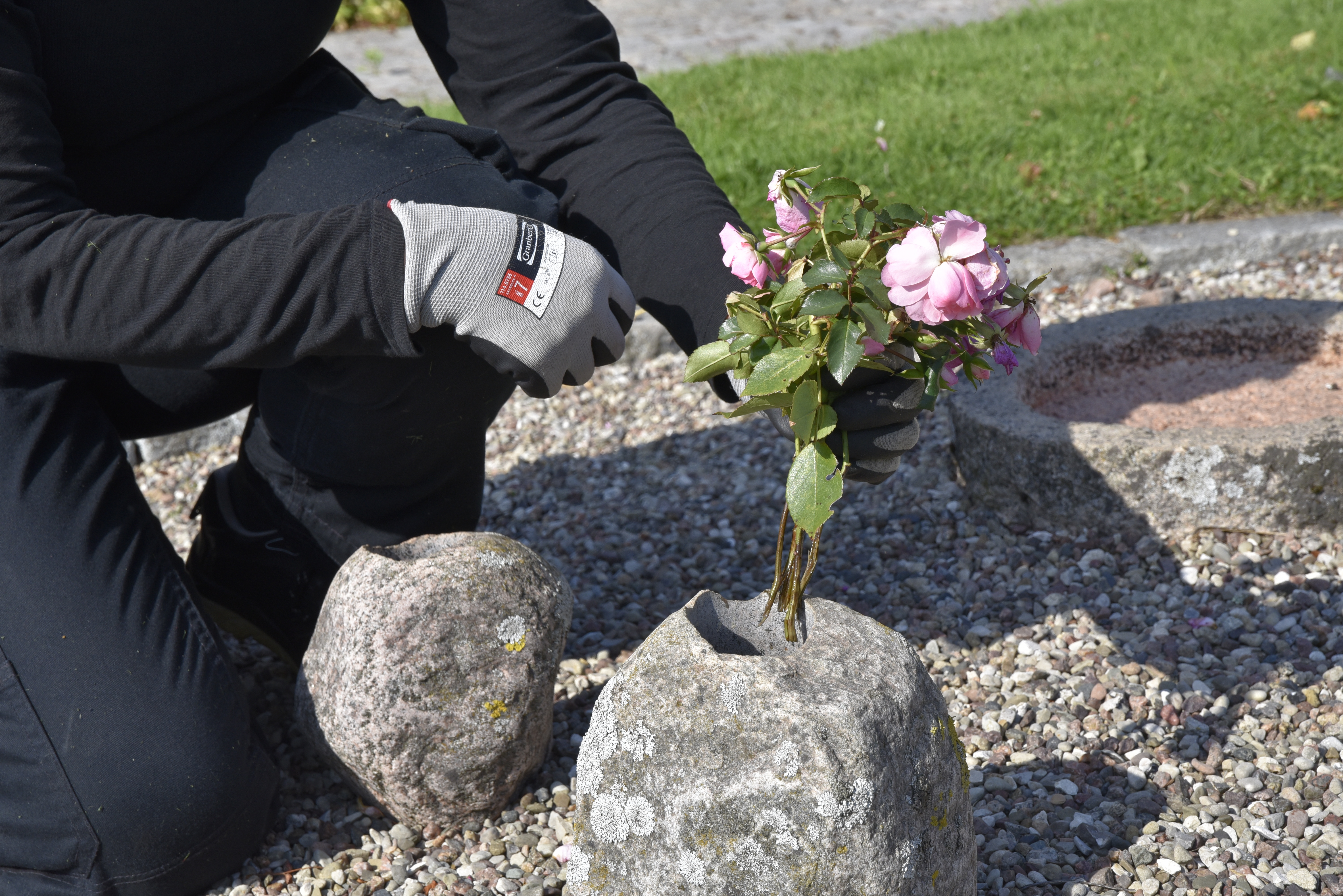 En person i trädgårdshandskar sitter hukad och håller i en blombukett