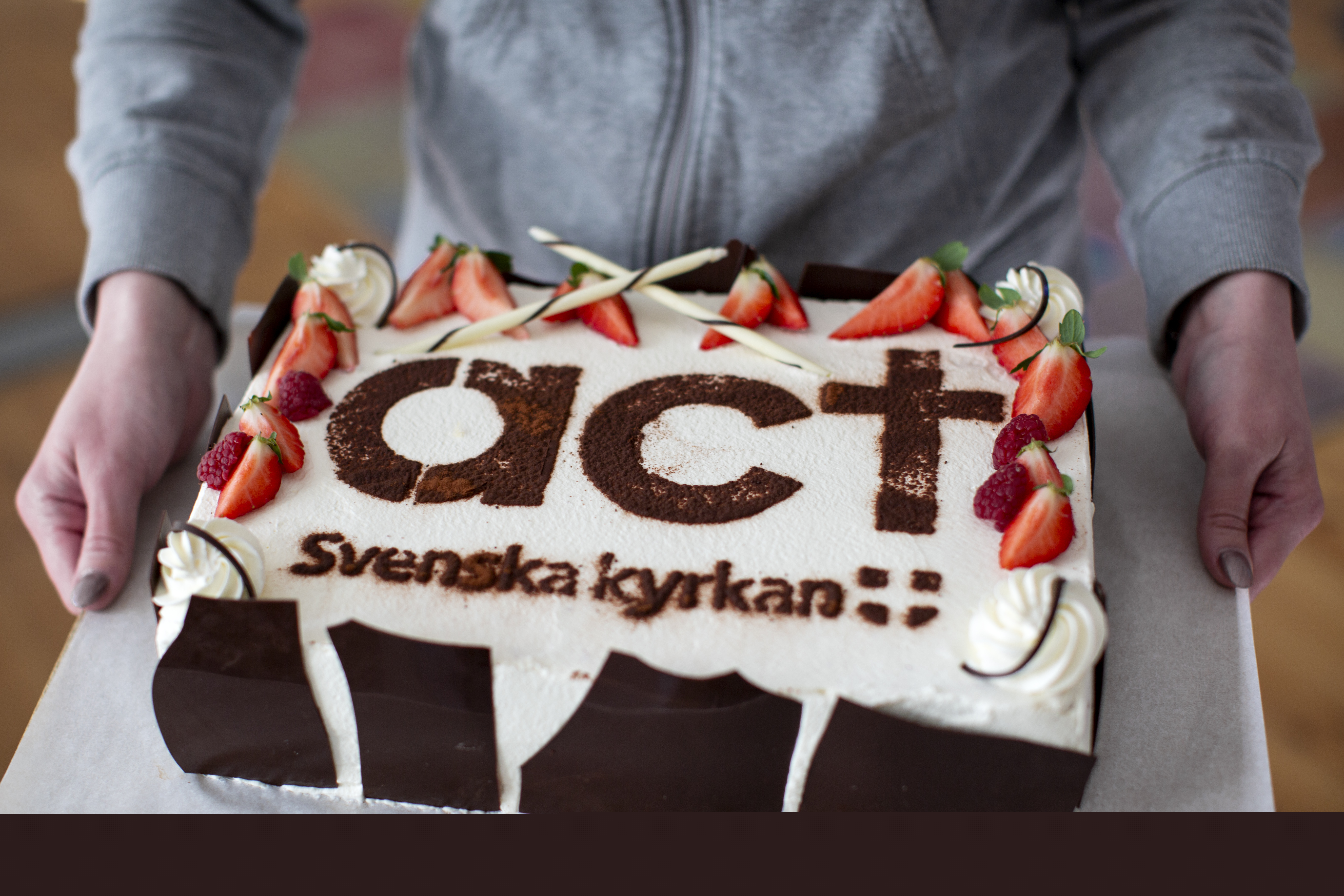 Tåtra med jordgubbar och grädde. På tårtan står det Act Svenska kyrkan.