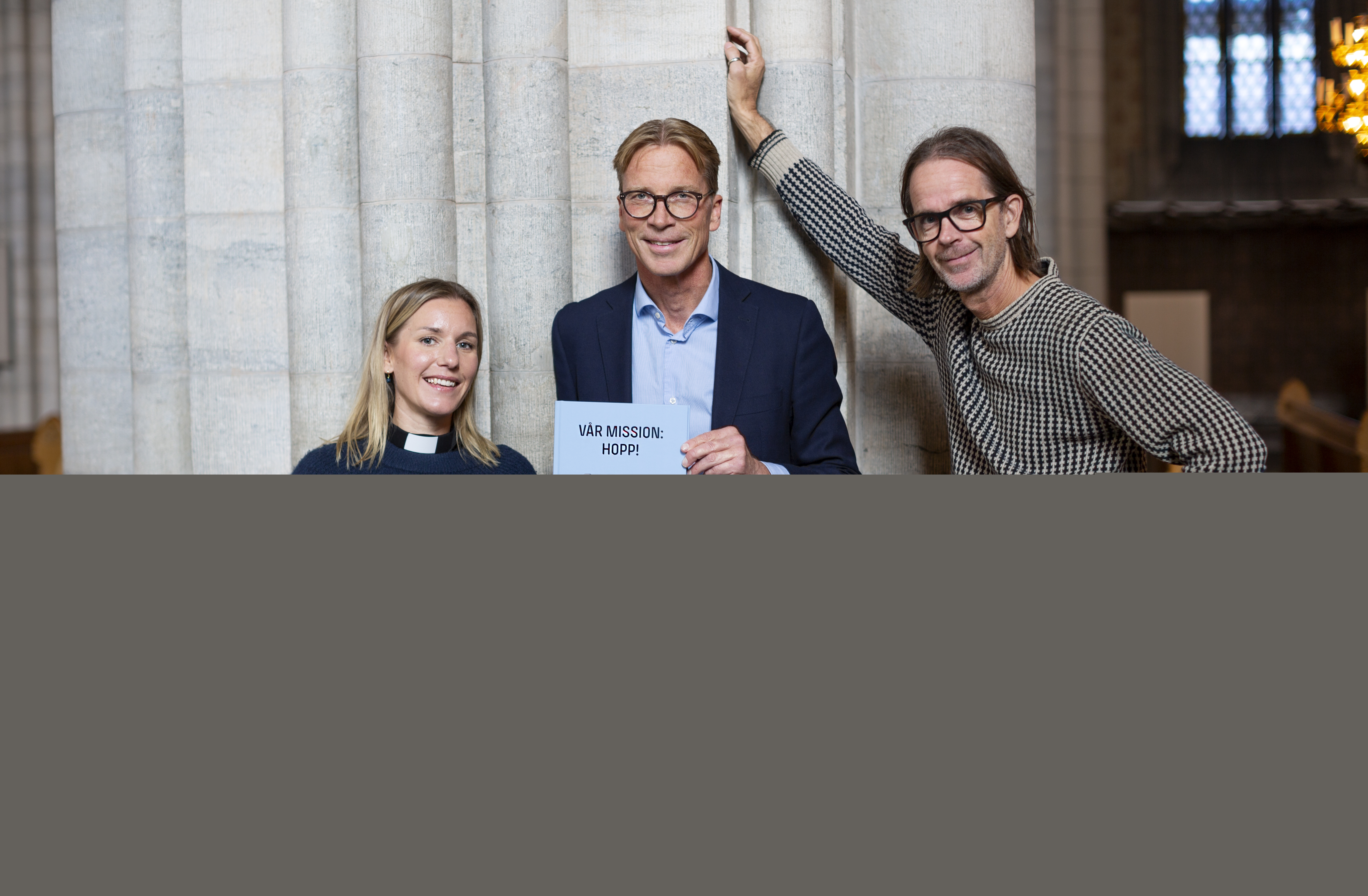 På bilden syns tre personer, personen i mitten håller i boken Vår mission: hopp!