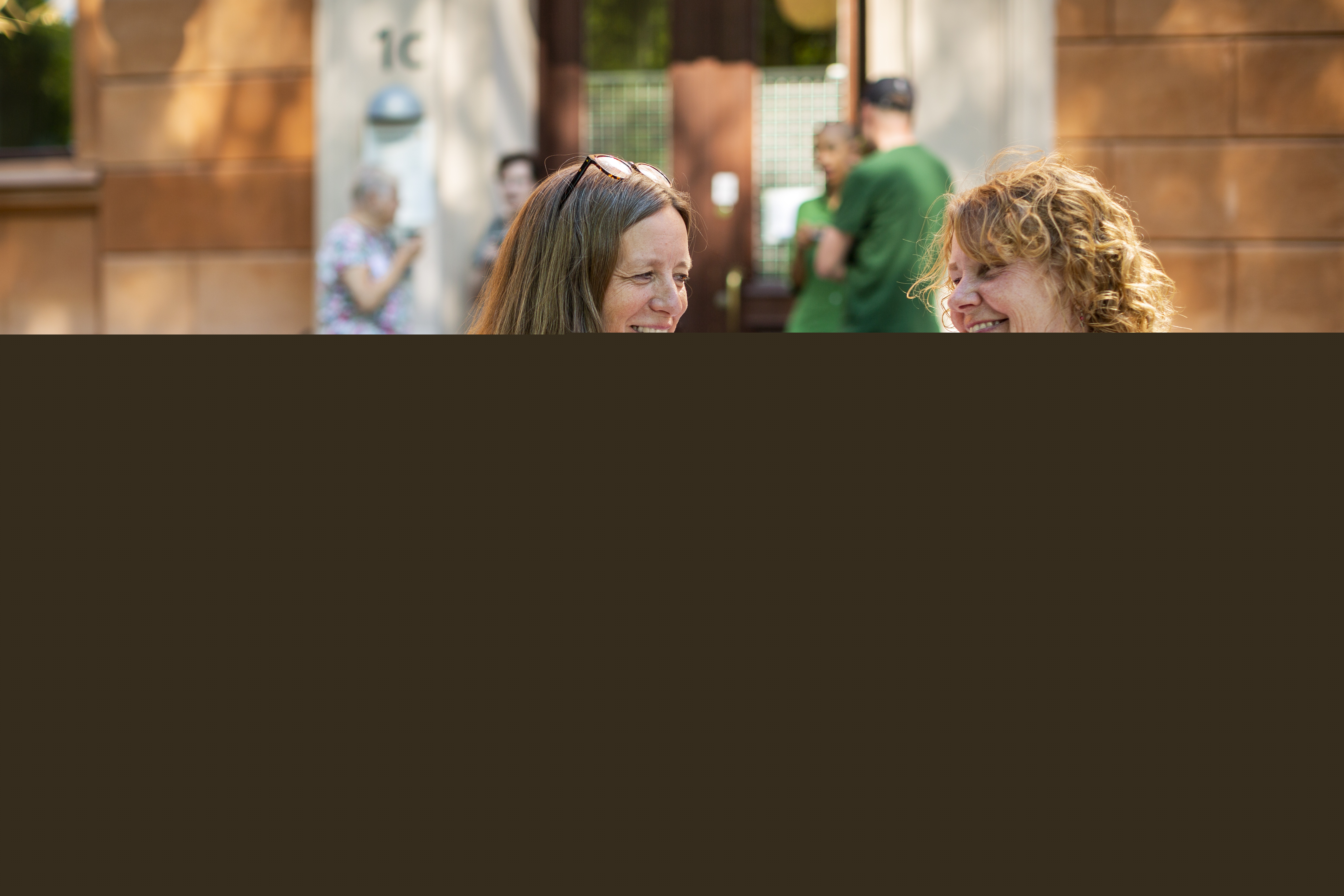 Två kvinnor ler mot varandra. Bakom dem syns fler människor i en trappa.