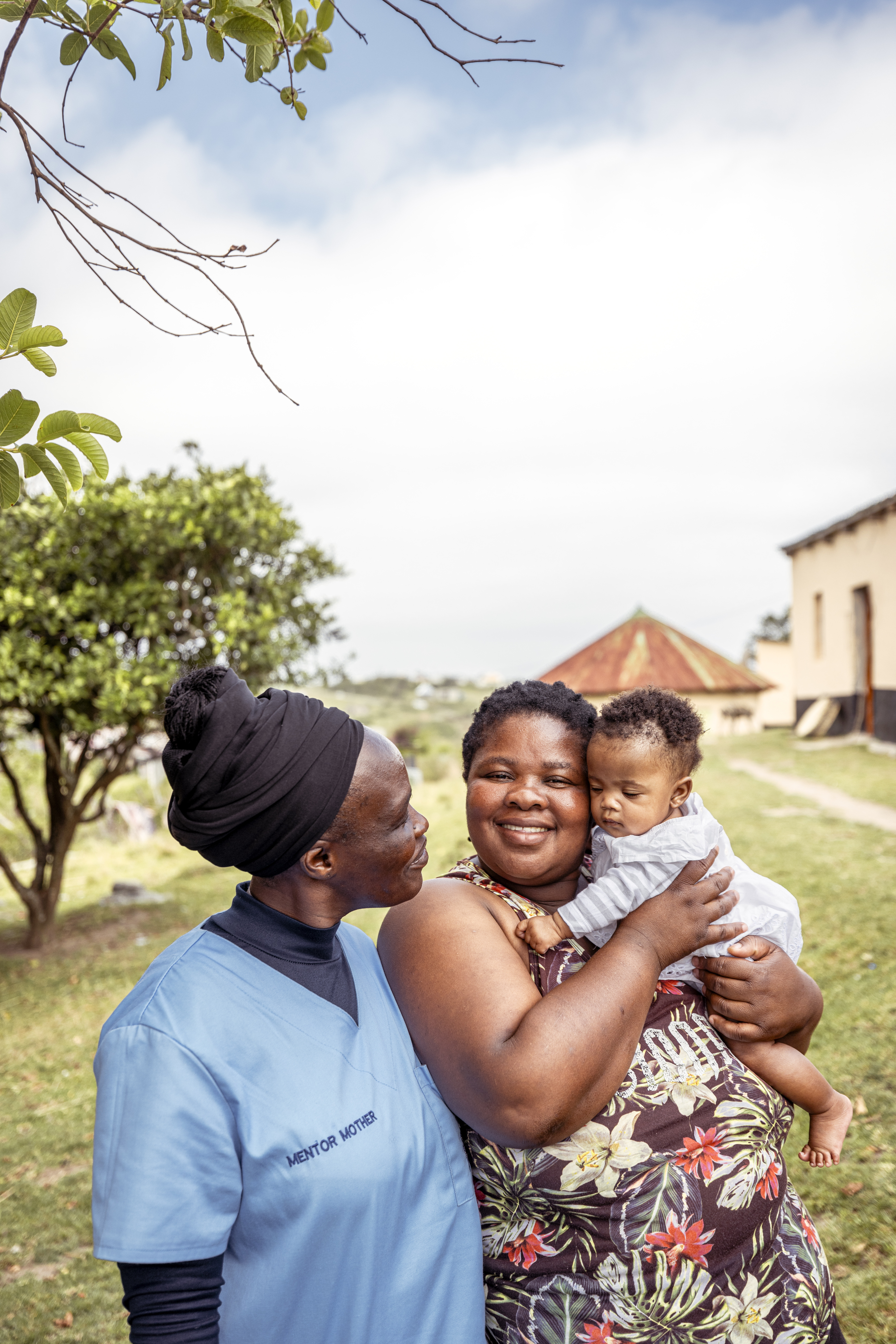 På bilden syns två kvinnor och en liten bebis. En av kvinnorna tittar in i kameran och ler. 