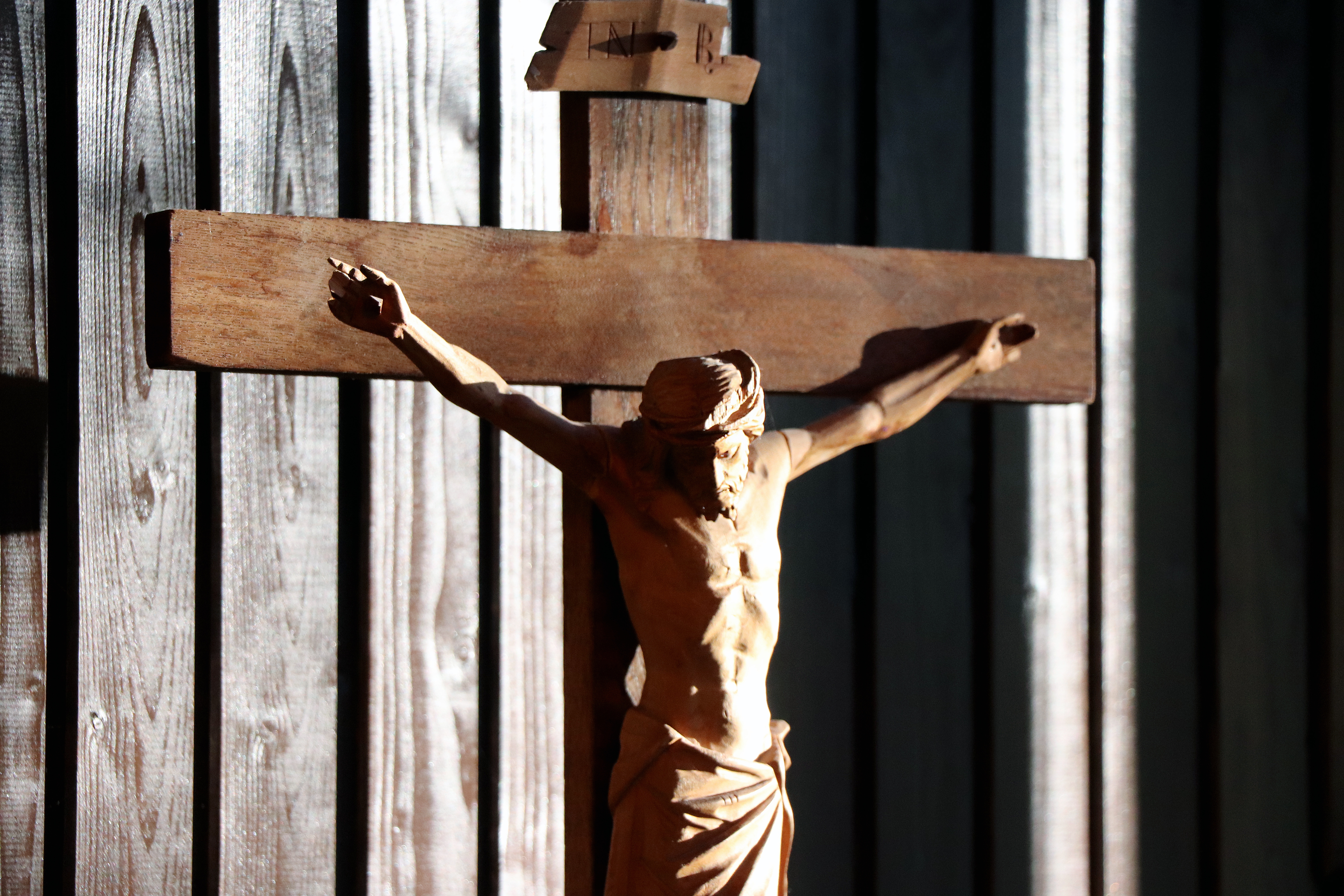 Solen skiner på ett träkrucifix mot träpanel i bakgrunden.