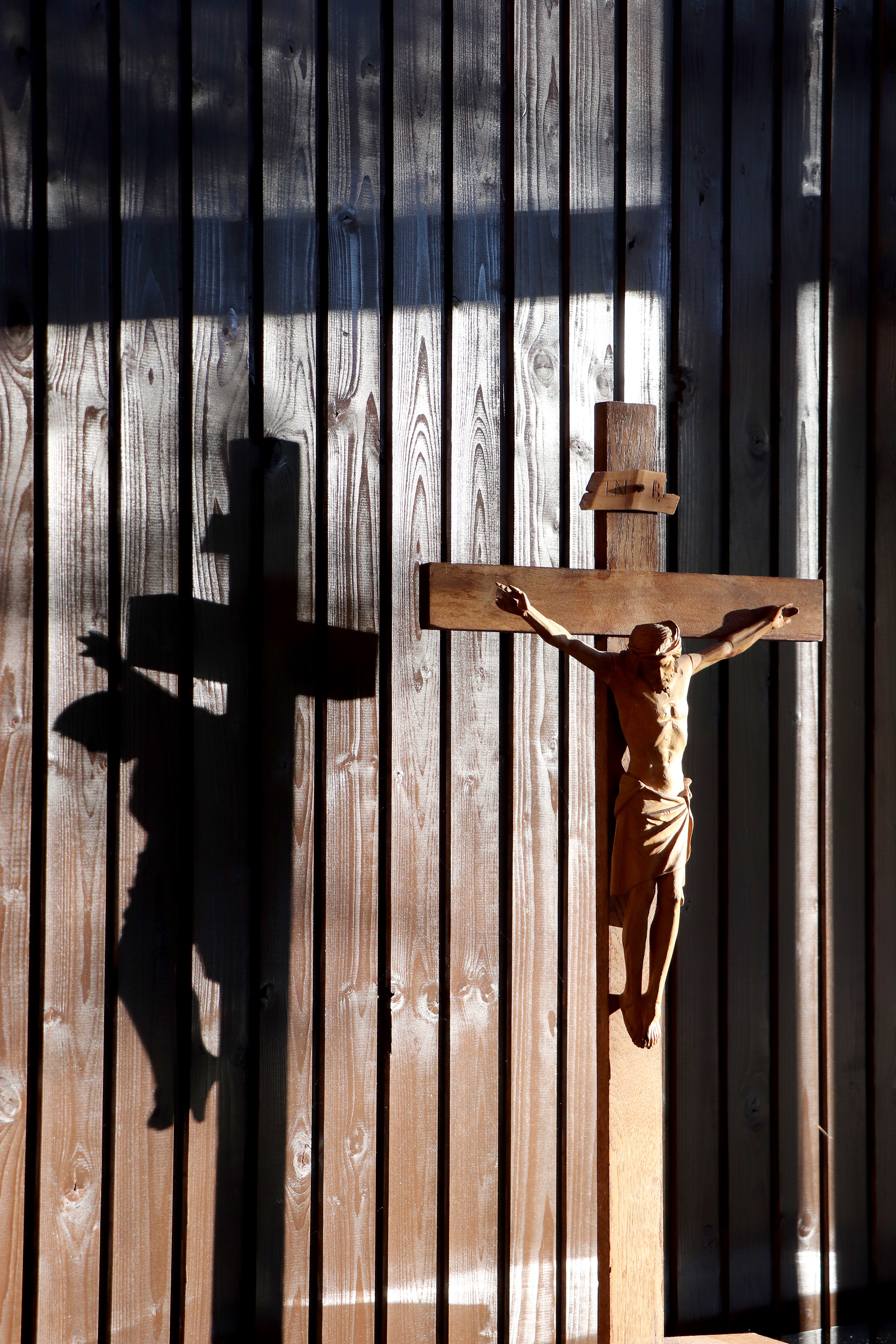 Solen skiner på ett träkrucifix mot träpanel i bakgrunden.