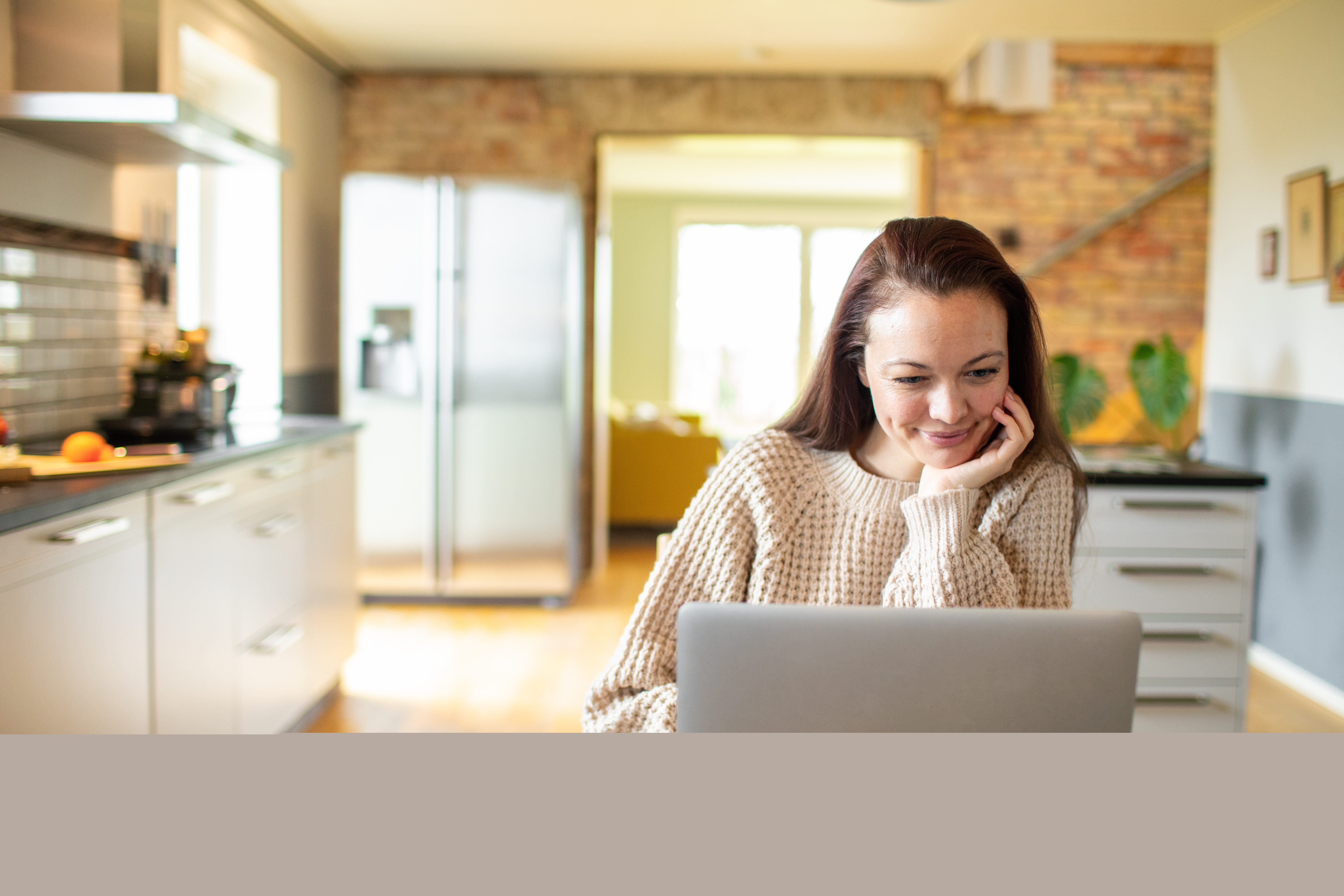 Ung kvinna som använder en bärbar dator i ett kök.