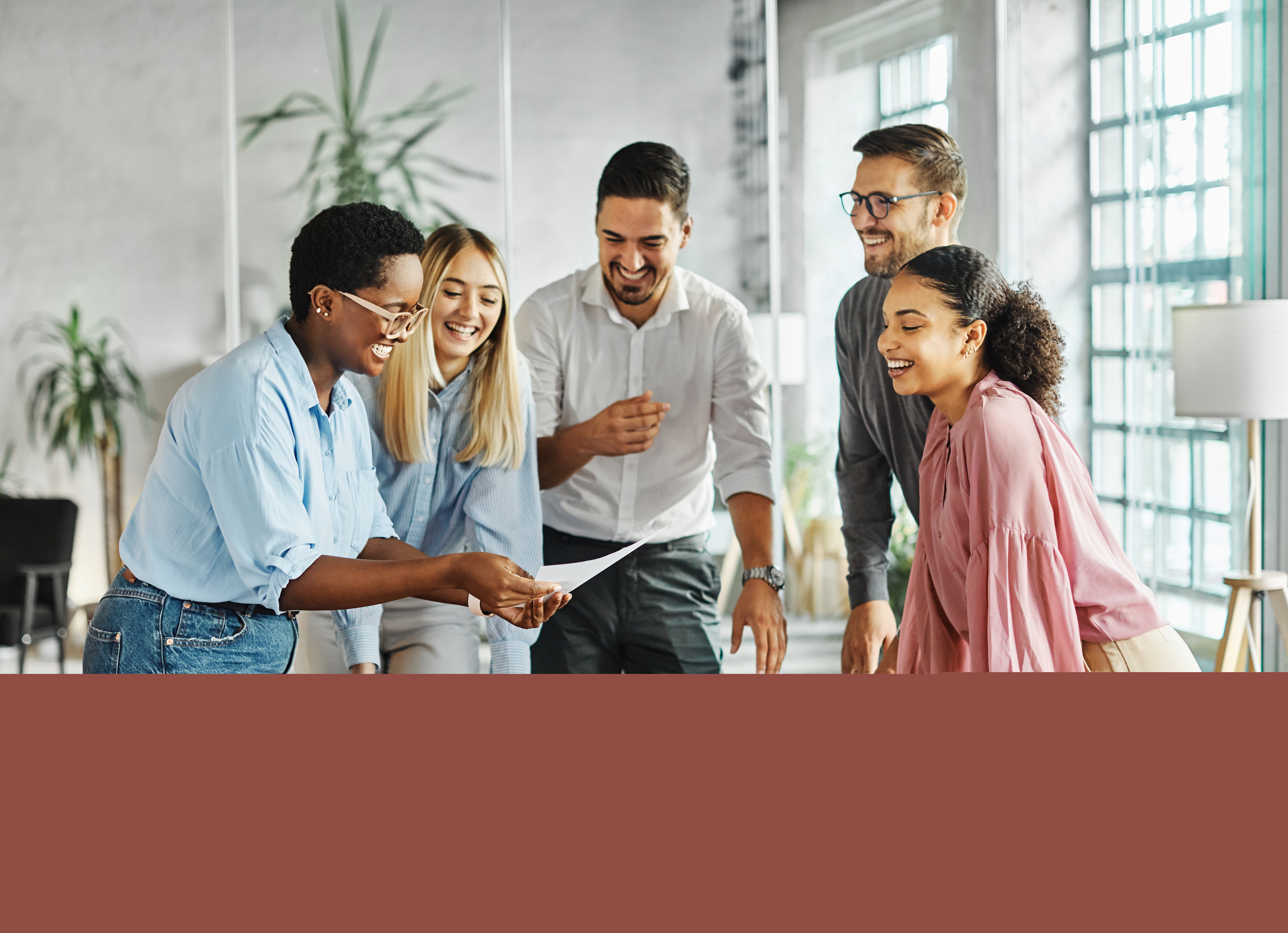 En grupp människor står runt ett bord och tittar på ett arbetsdokument med glada miner.